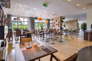 A spacious hotel lobby with multiple dining areas, a reception desk, and large windows offering a view of the outdoors. - Mercure Hotel Kamen Unna (Kamen)