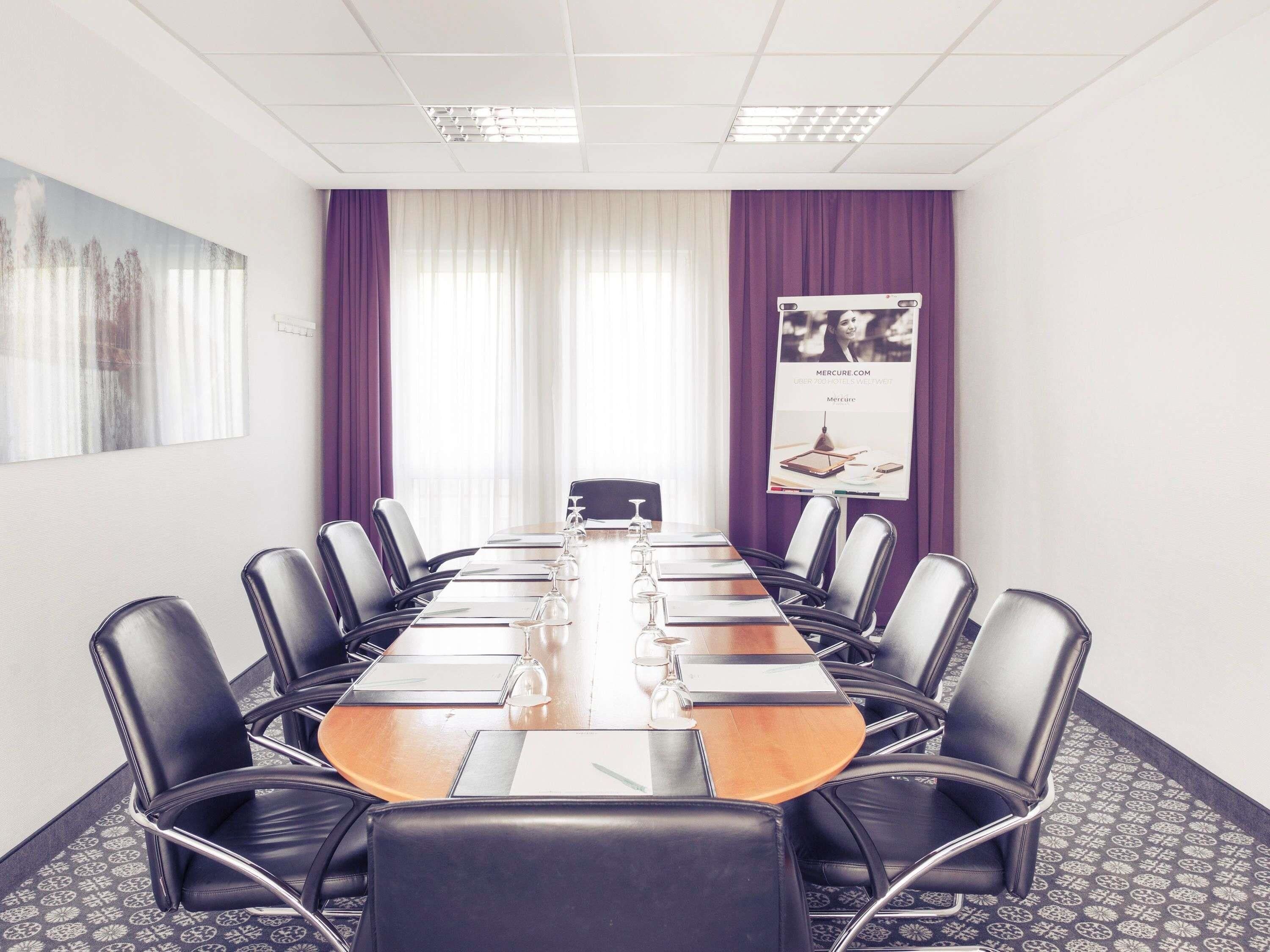 A conference room with a long table, black leather chairs, and a banner on the wall.