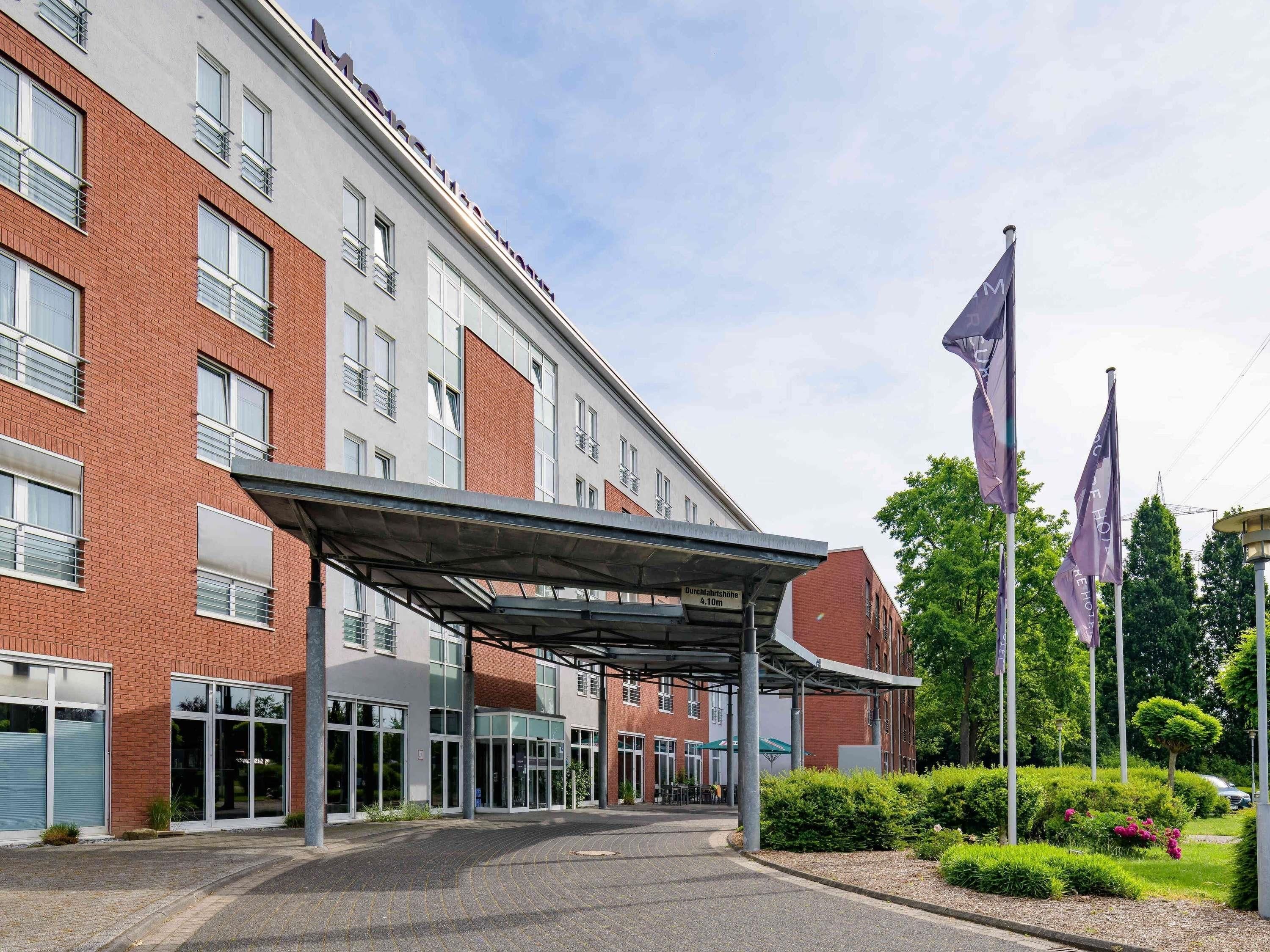 A modern hotel entrance with a covered walkway, large windows, and a clear sky.