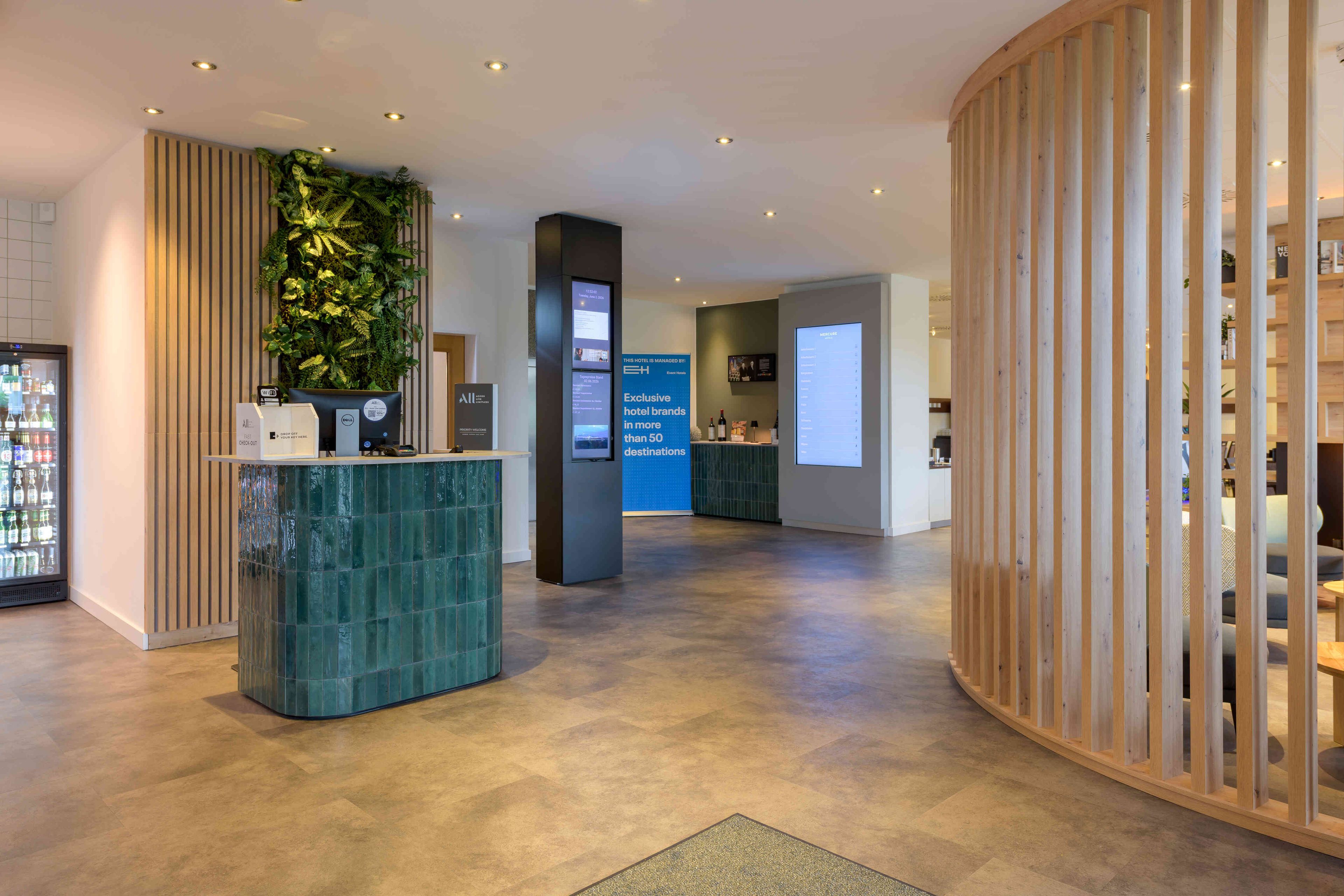 A hotel reception area with a modern design, including a reception desk, a digital display board, and a plant wall.