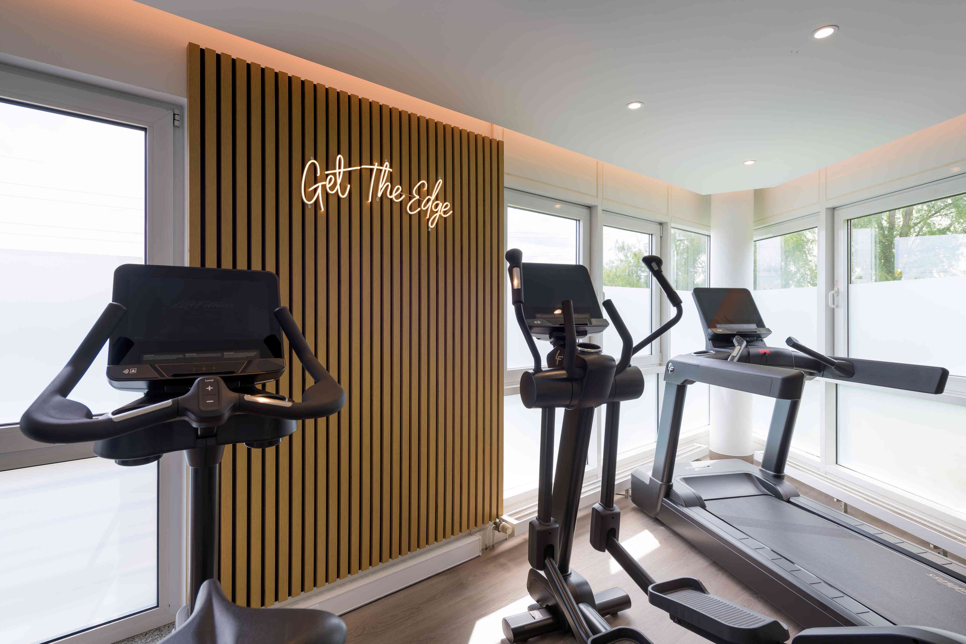 A gym with stationary bikes, treadmills, and a wooden wall with a neon sign.