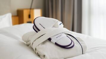 A neatly folded white towel with a purple trim and a Mercure hotel tag on a bed.