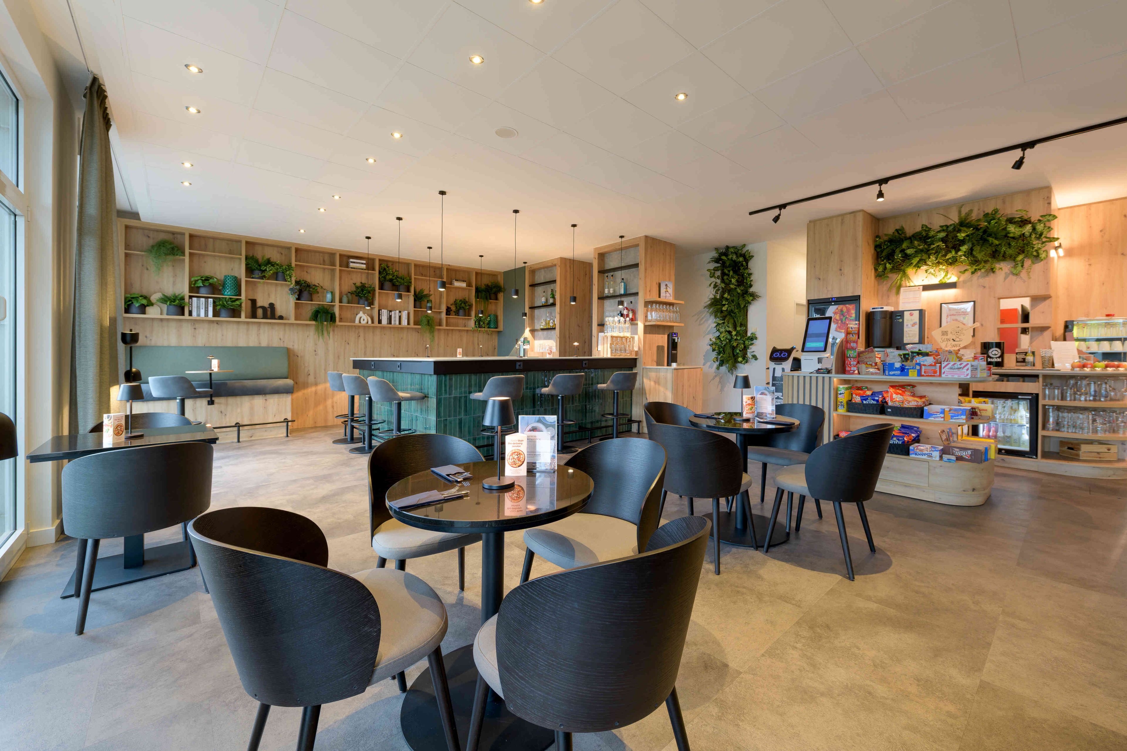 Ein modernes Café mit runden Tischen und Stühlen, einer Bar und Regalen mit Pflanzen und Getränken.