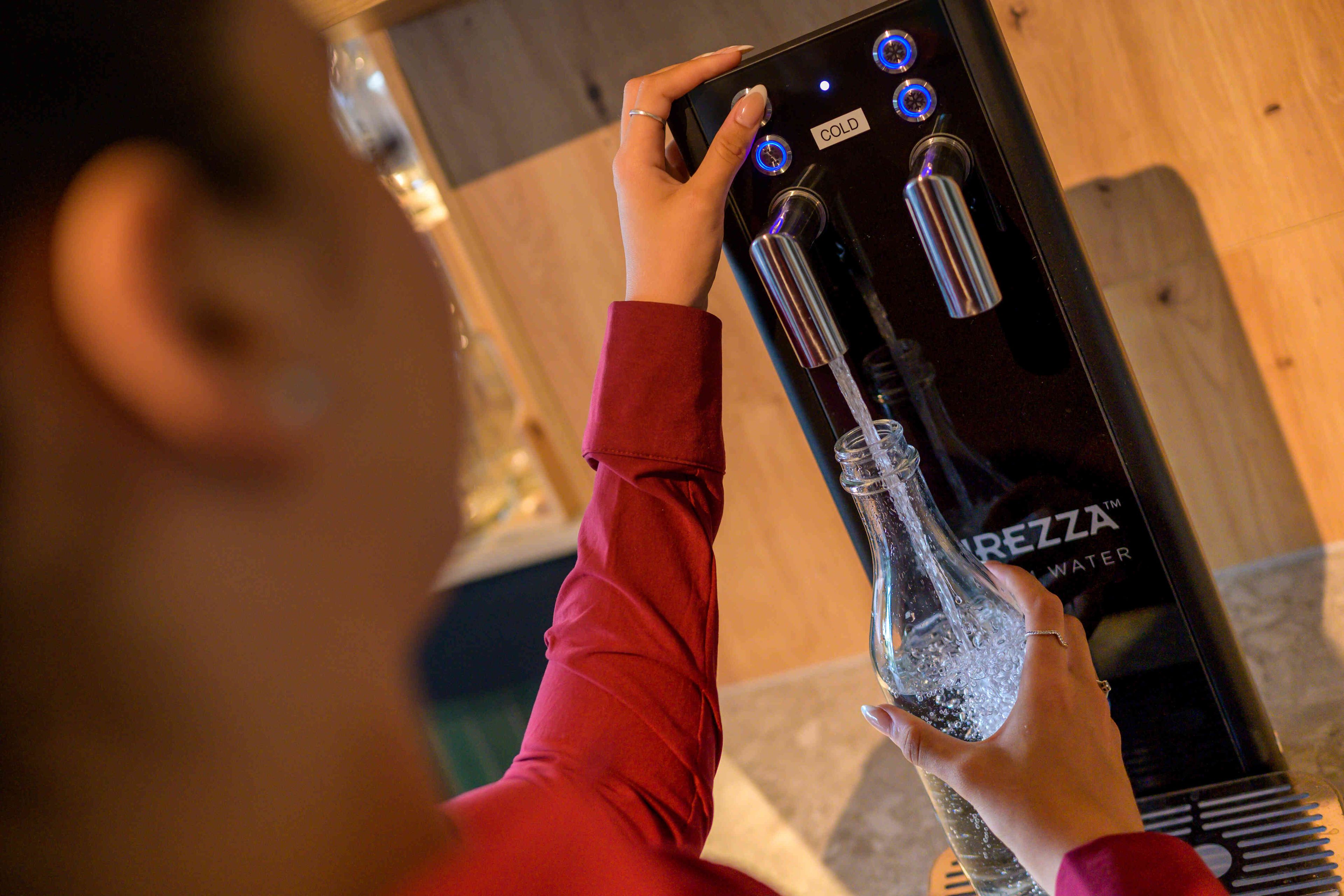 A person using a water dispenser with a bottle in hand.