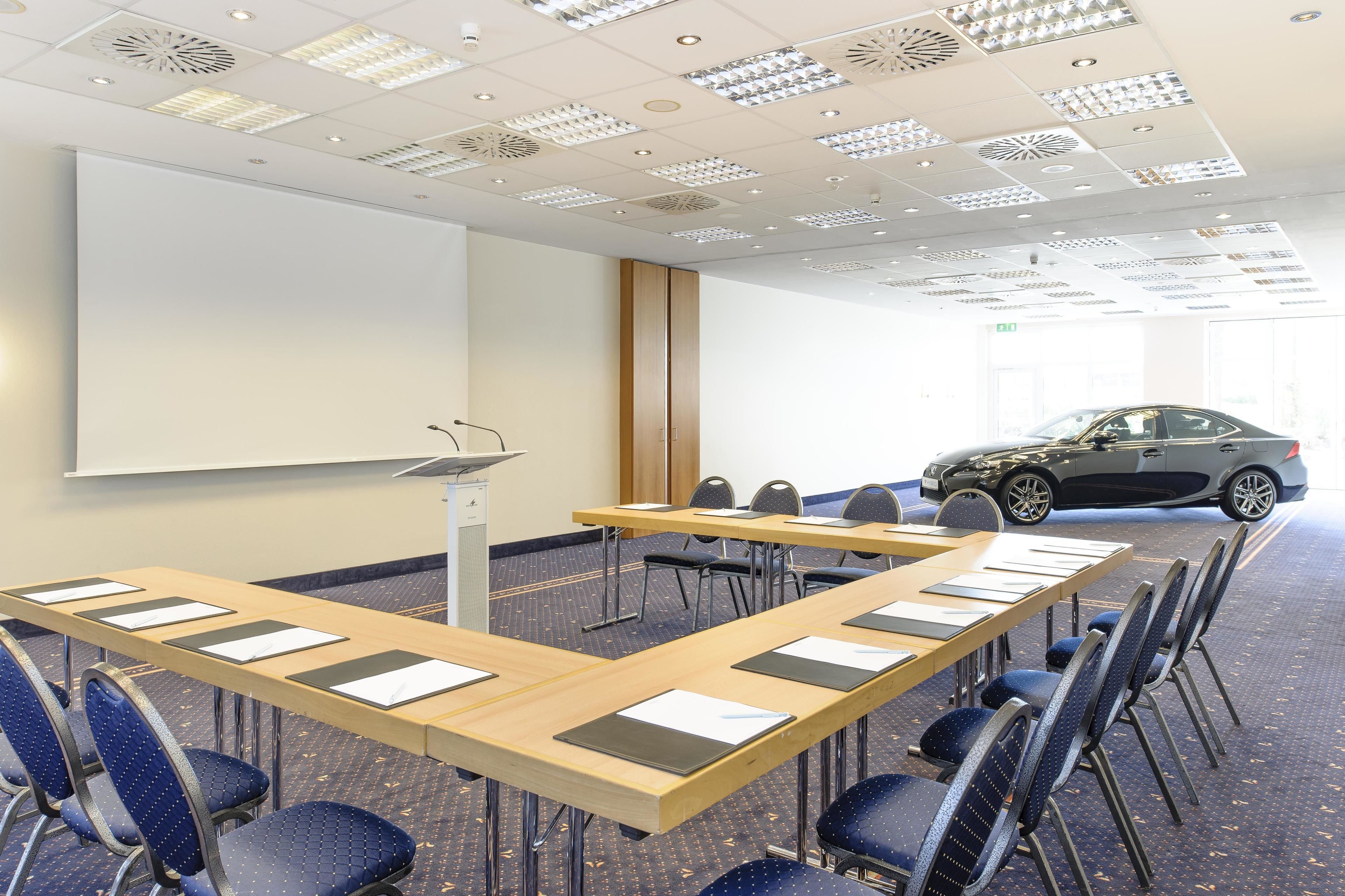 A conference room with a large table, chairs, a projector screen, and a car parked outside.