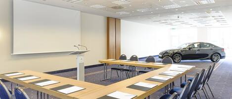 A conference room with a large table, chairs, a projector screen, and a car parked outside.