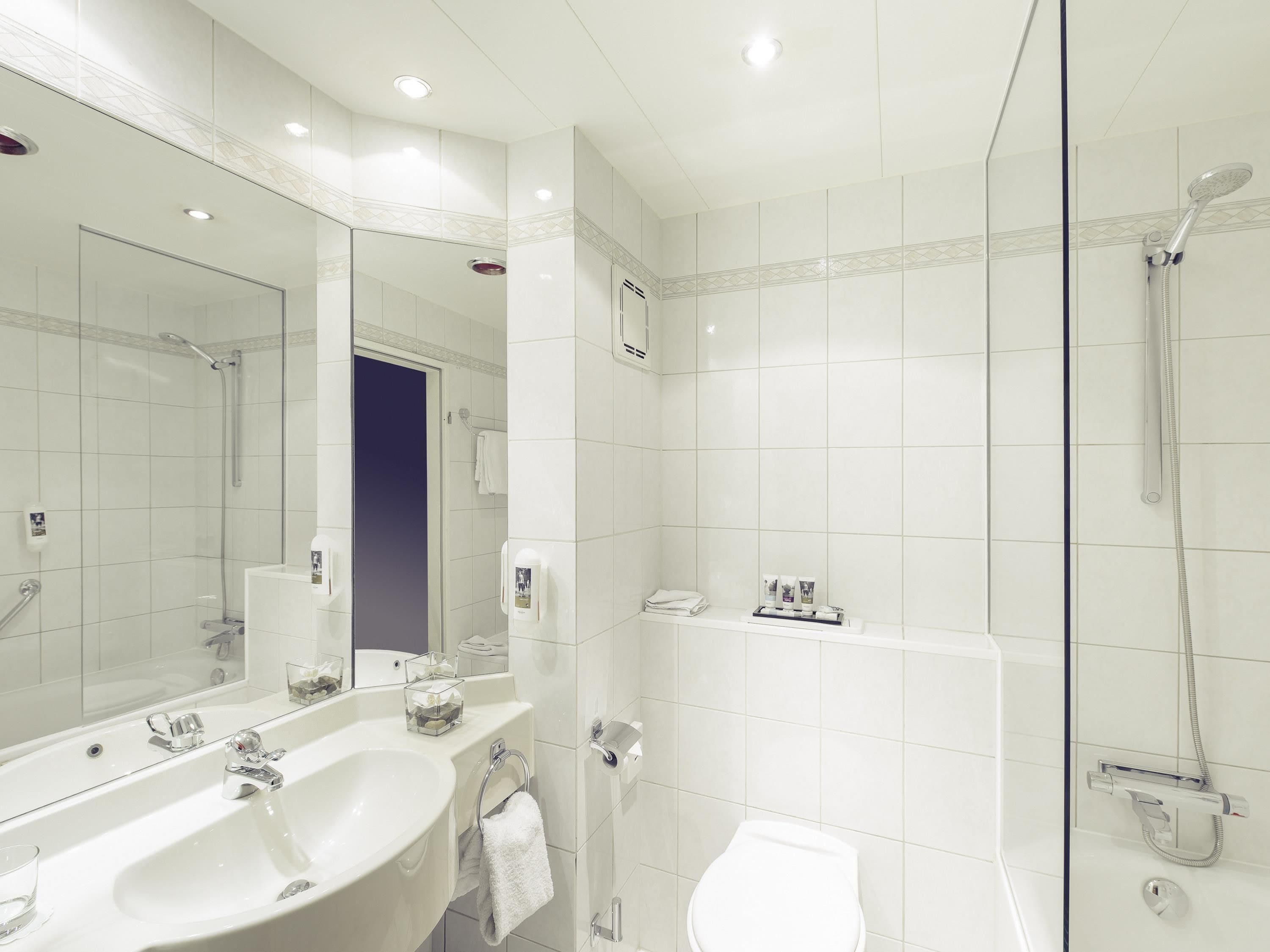 A modern bathroom with a large mirror, a sink, a toilet, and a shower.
