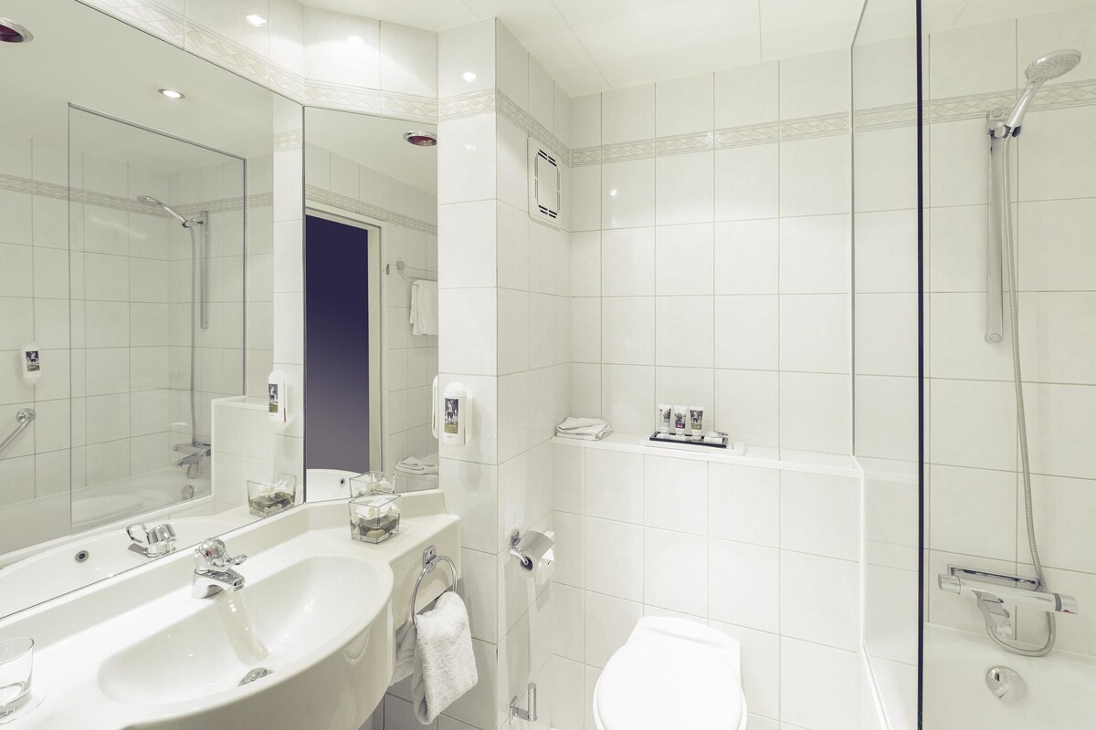 A modern bathroom with a large mirror, a sink, a toilet, and a shower.