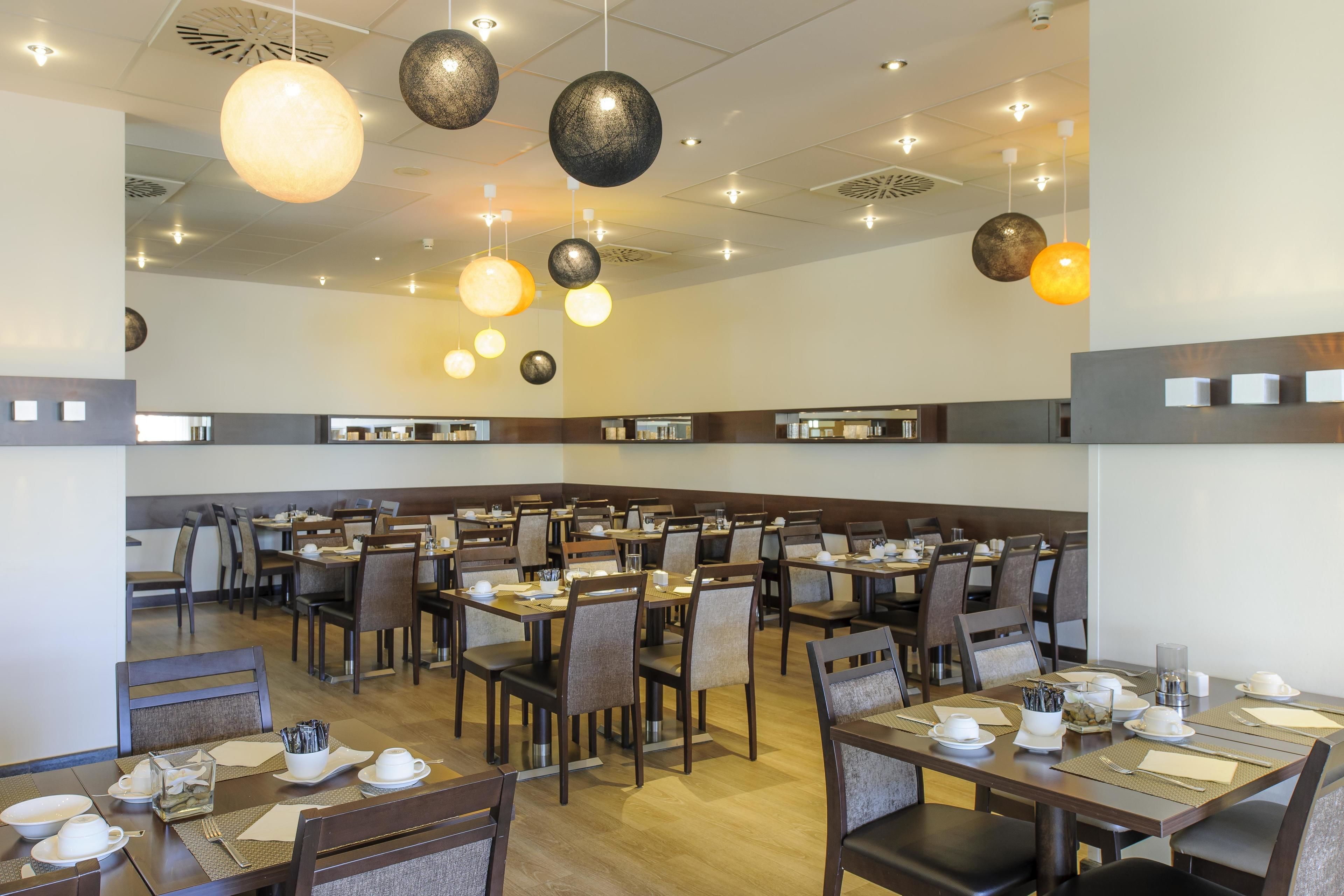 Un comedor amplio con varias mesas y sillas, lámparas colgantes e iluminación, y un diseño limpio y moderno.