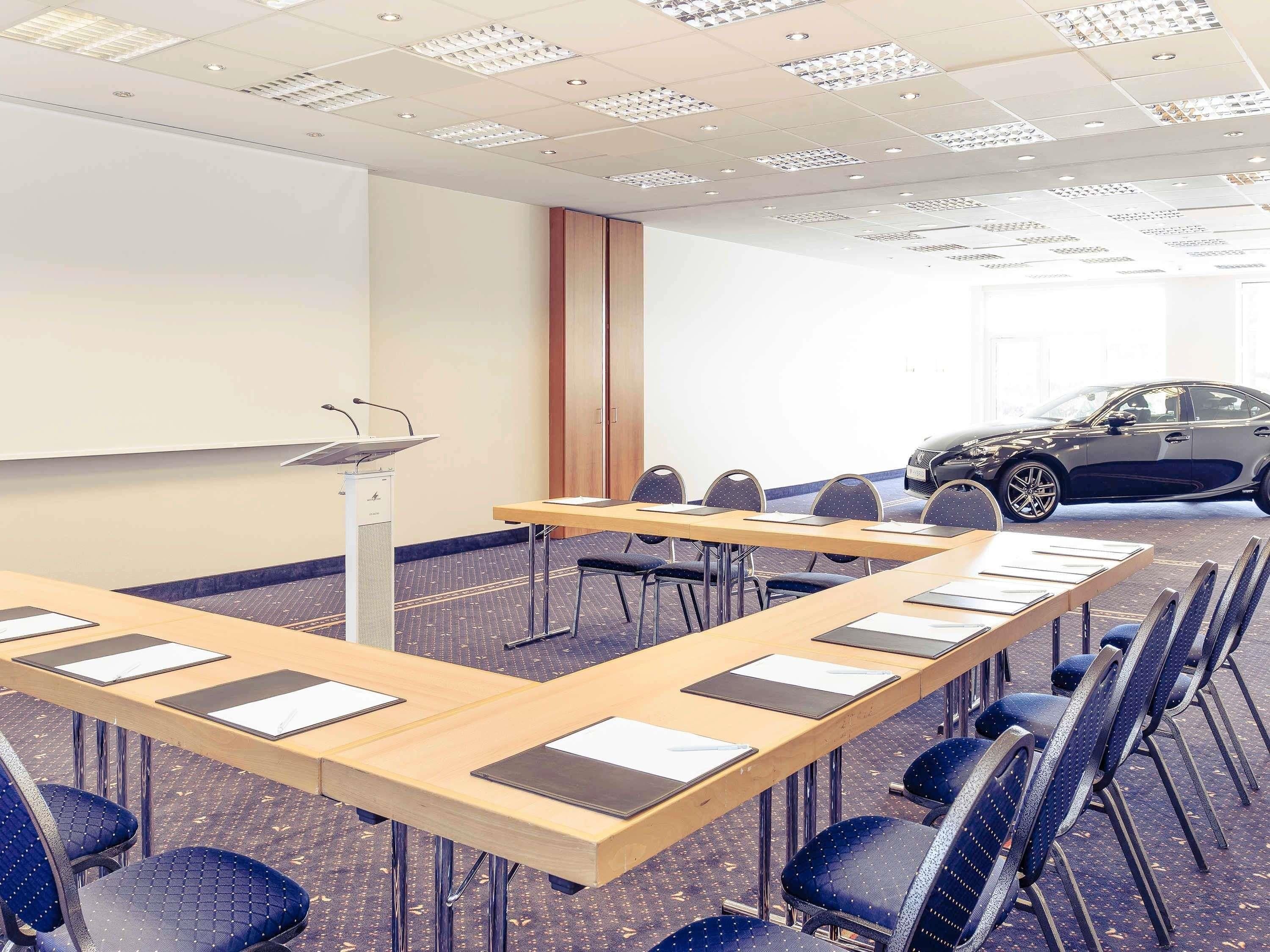 A conference room with a long table, chairs, a podium, and a projector screen.