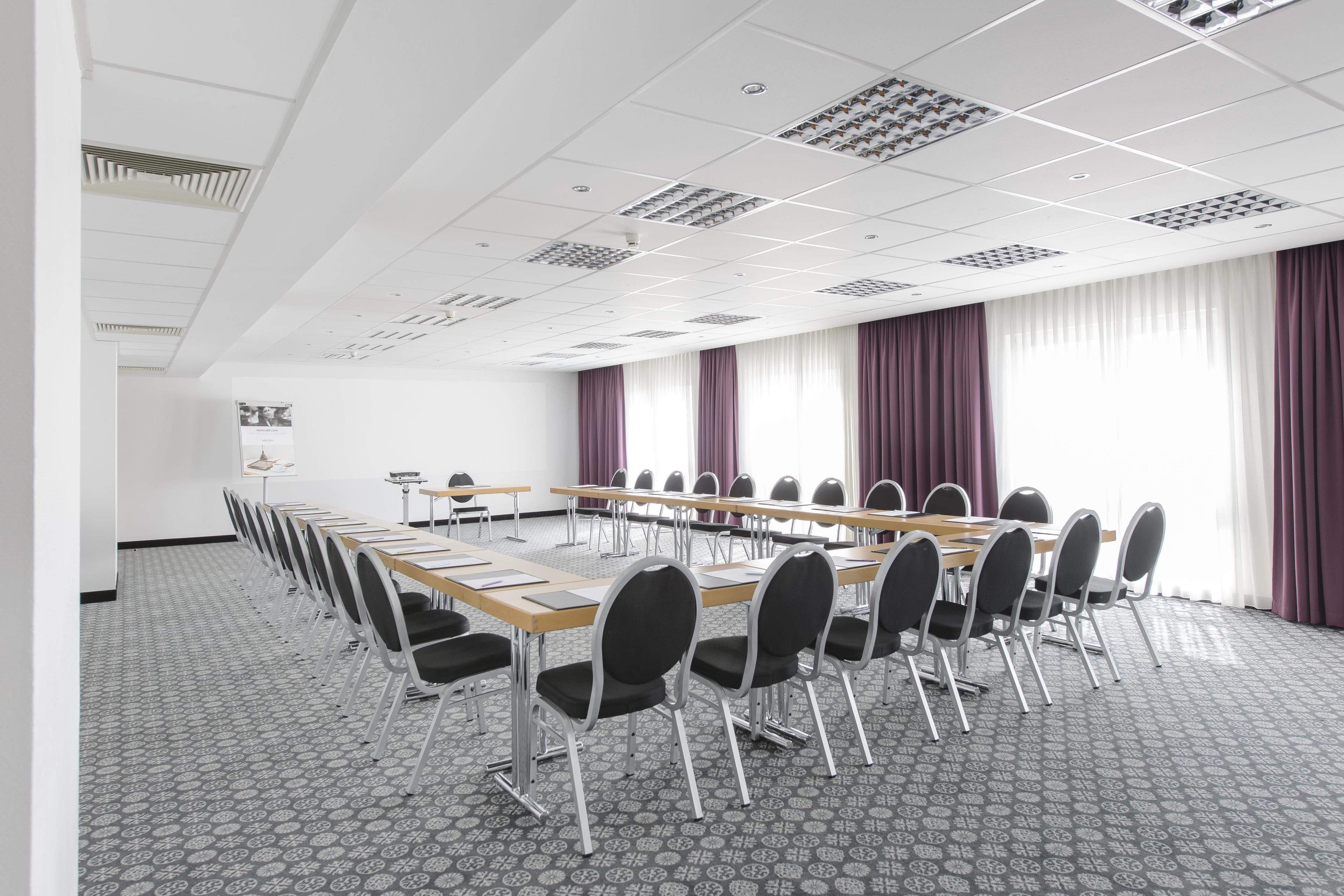 Un salón de conferencias con una larga mesa, sillas y una alfombra estampada.