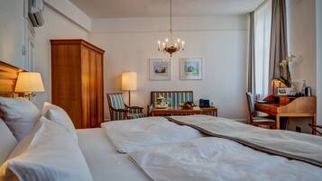 Habitación de hotel con una cama grande, un escritorio, una silla, una lámpara y dos cuadros en la pared.