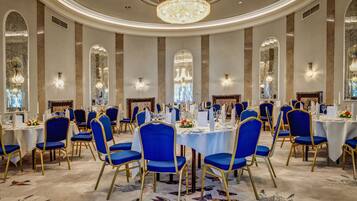 Un comedor elegante con mesas redondas, sillas tapizadas en azul y candelabros.