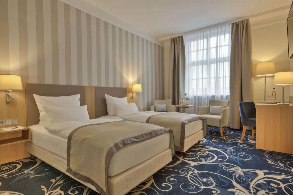 A hotel room with two beds, a desk, a chair, and a small table.