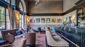 Una zona de bar con asientos, una barra con botellas y obras de arte enmarcadas en la pared.