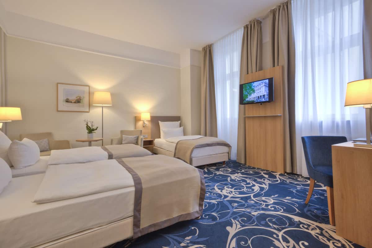 A hotel room with two beds, a desk, a chair, a TV, and a patterned carpet.