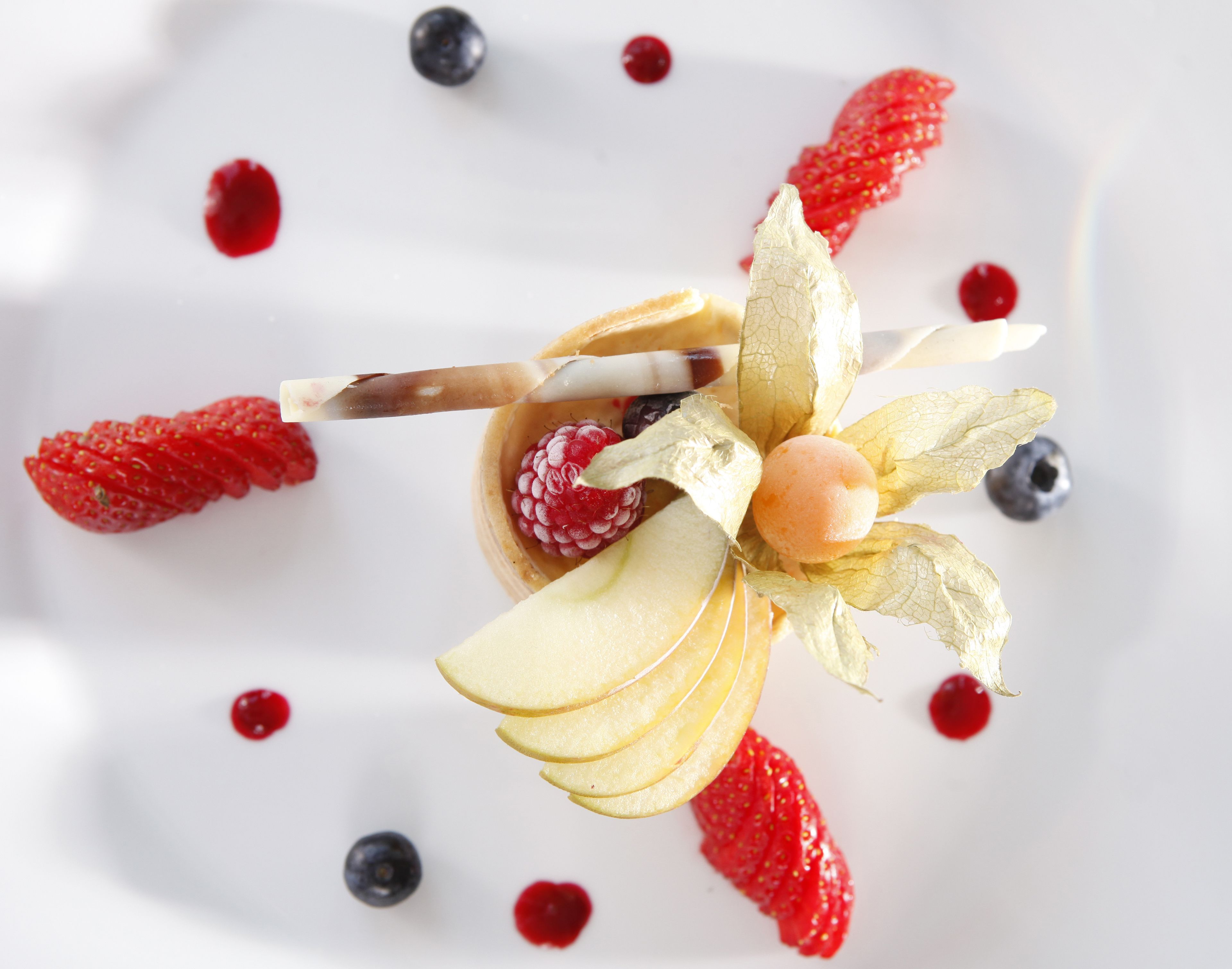 Dessert mit Obst und einer dekorativen Verzierung auf einem weißen Teller.