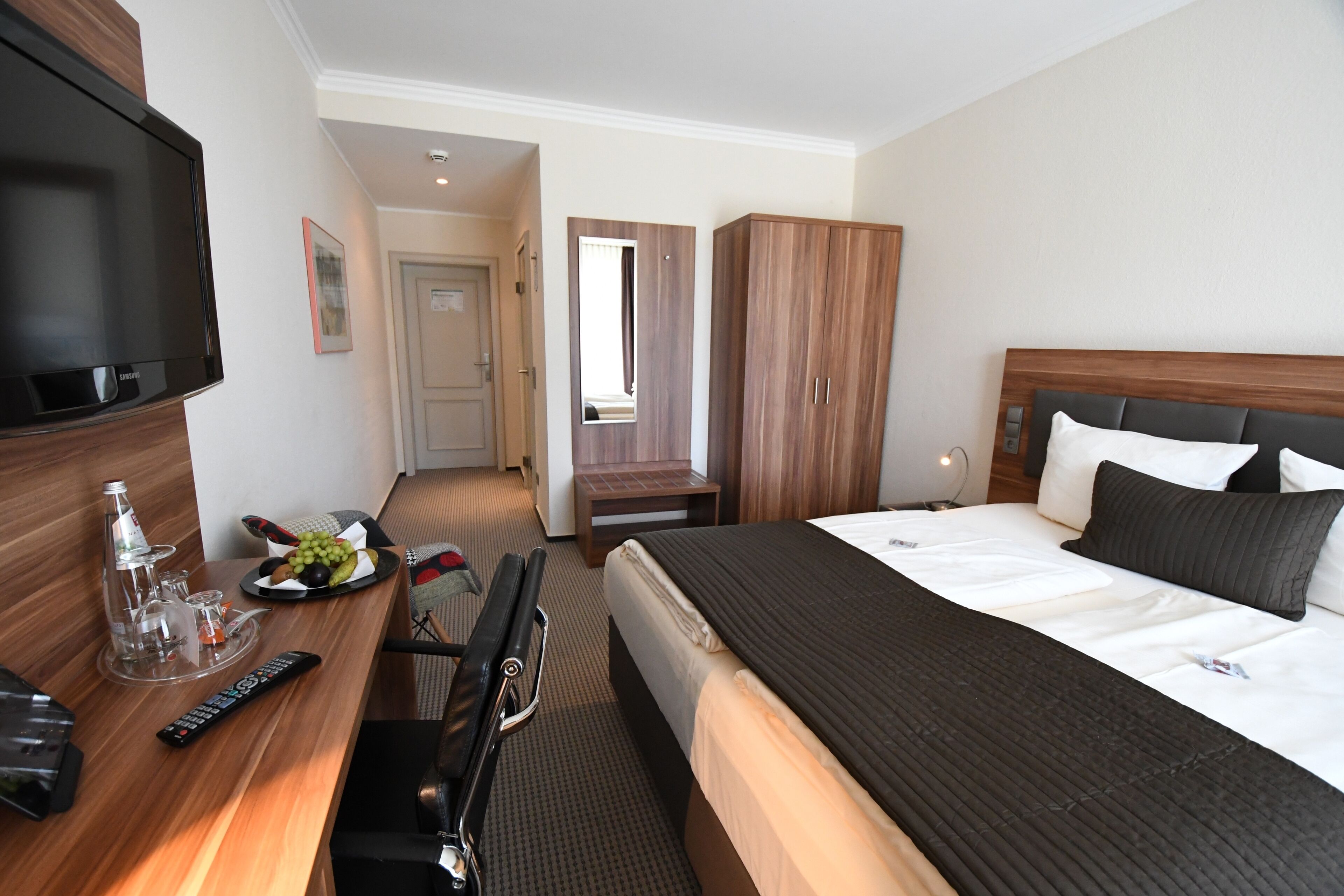 Ein Hotelzimmer mit Bett, Fernseher, Schreibtisch mit Fernbedienung, Spiegel und Kleiderschrank.