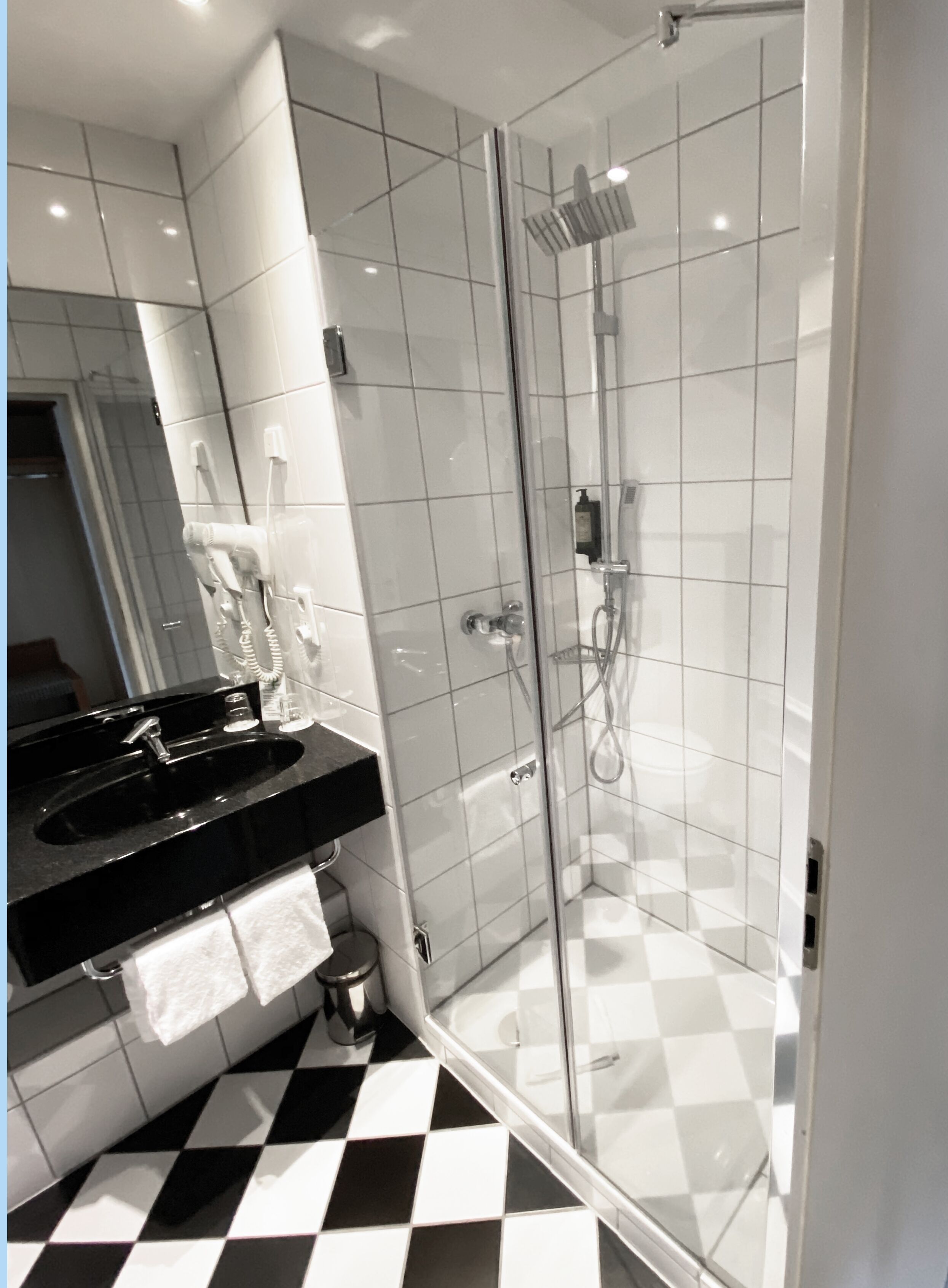 A modern bathroom with a black and white checkered floor, a glass-enclosed shower, and a black countertop with a sink and towel rack.