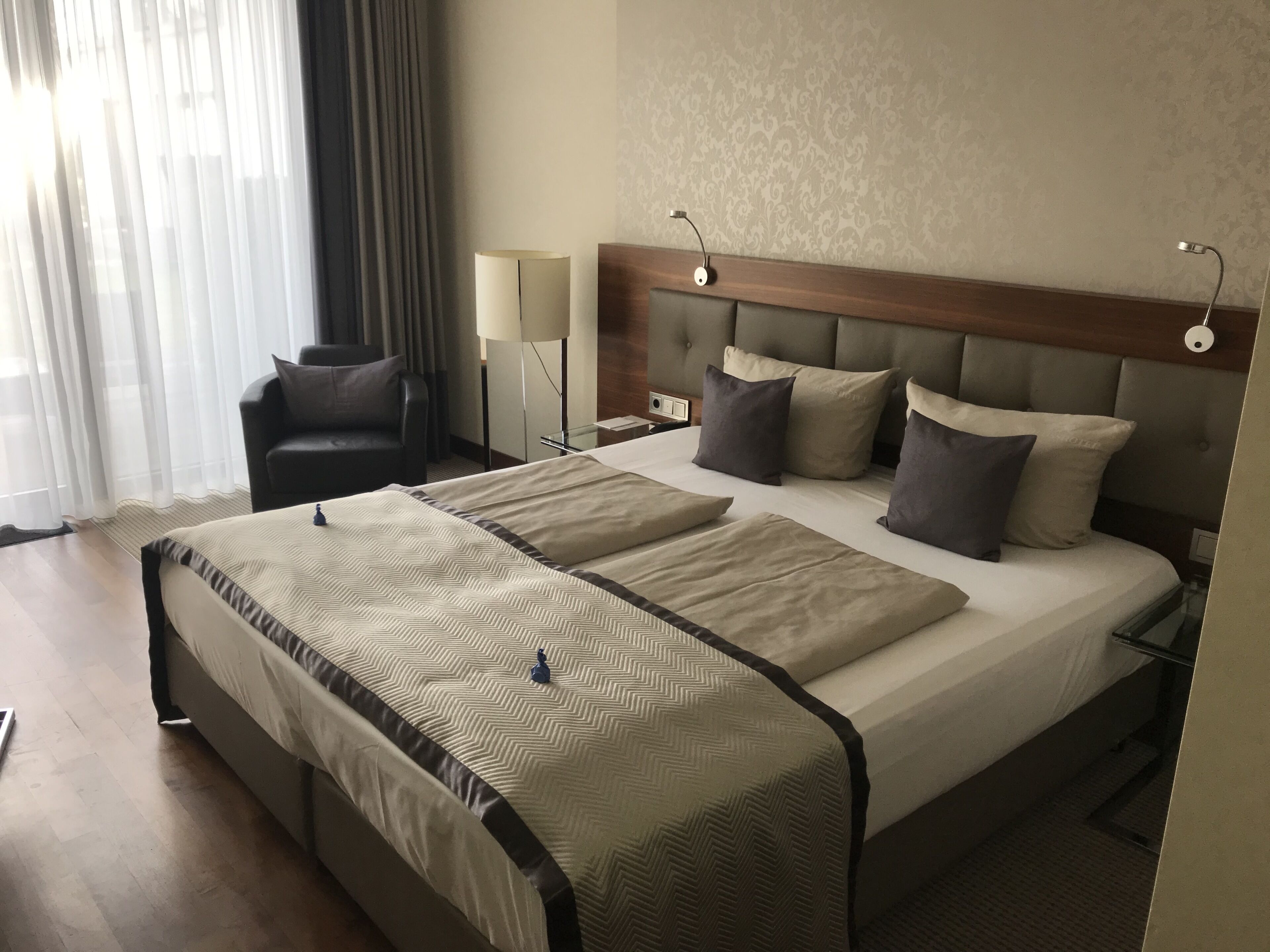 Una habitación de hotel con una cama grande, una silla, una mesita de noche y una lámpara.