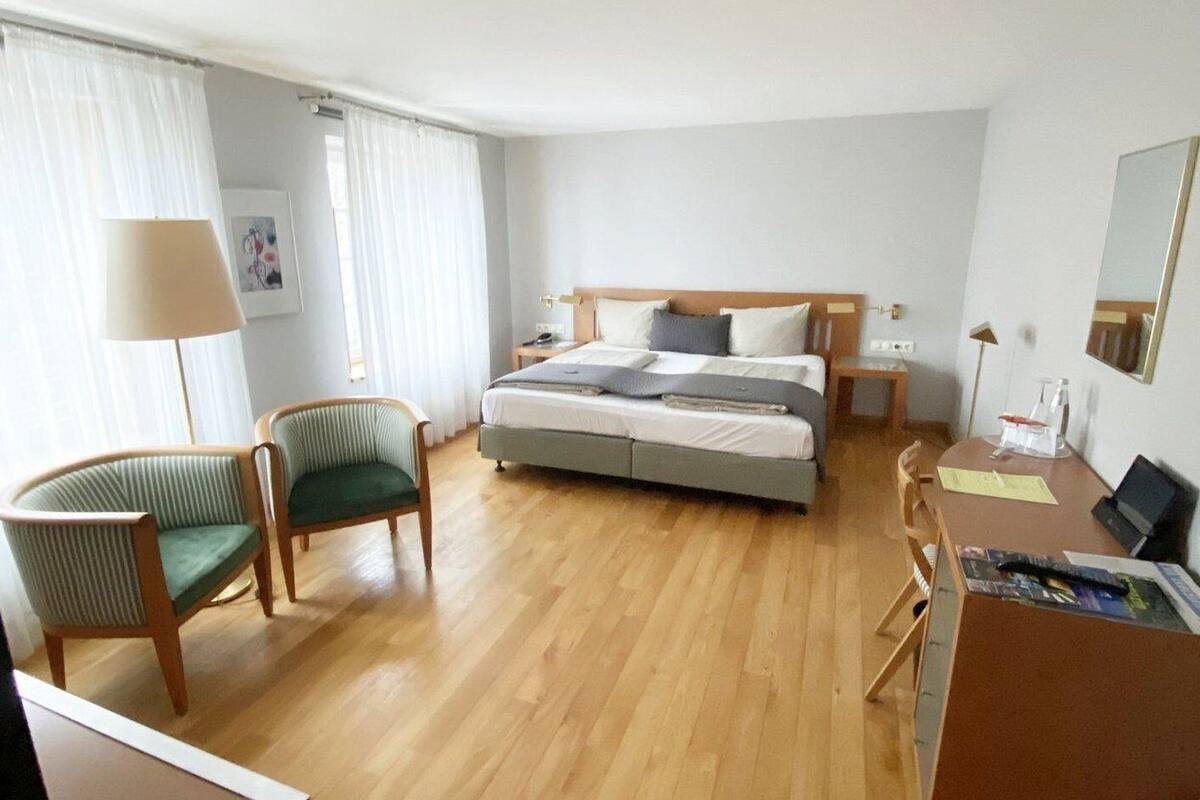 Ein Hotelzimmer mit einem Bett, zwei Stühlen, einem Schreibtisch, einer Lampe und einem Spiegel.