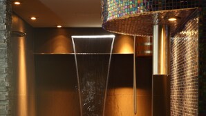 Un baño moderno con ducha envuelta en vidrio, pared de mosaicos curvada y suelo de madera.