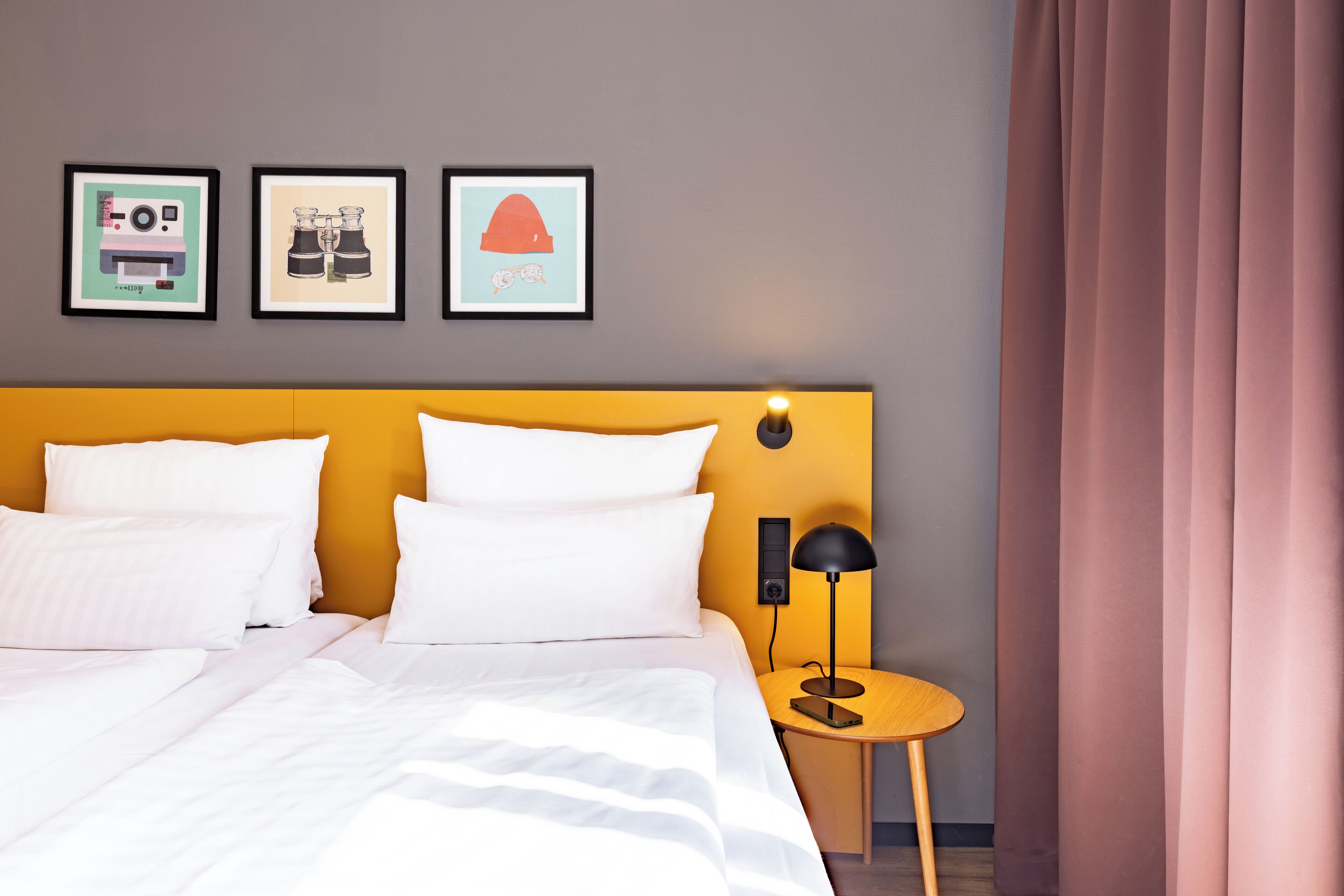 A hotel room with a bed, a bedside table with a lamp, and three framed pictures on the wall.