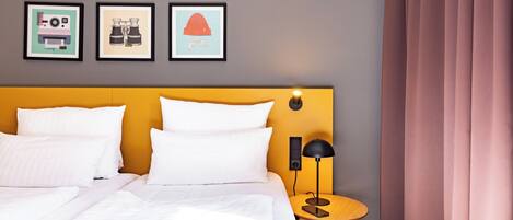 A hotel room with a bed, a bedside table with a lamp, and three framed pictures on the wall.