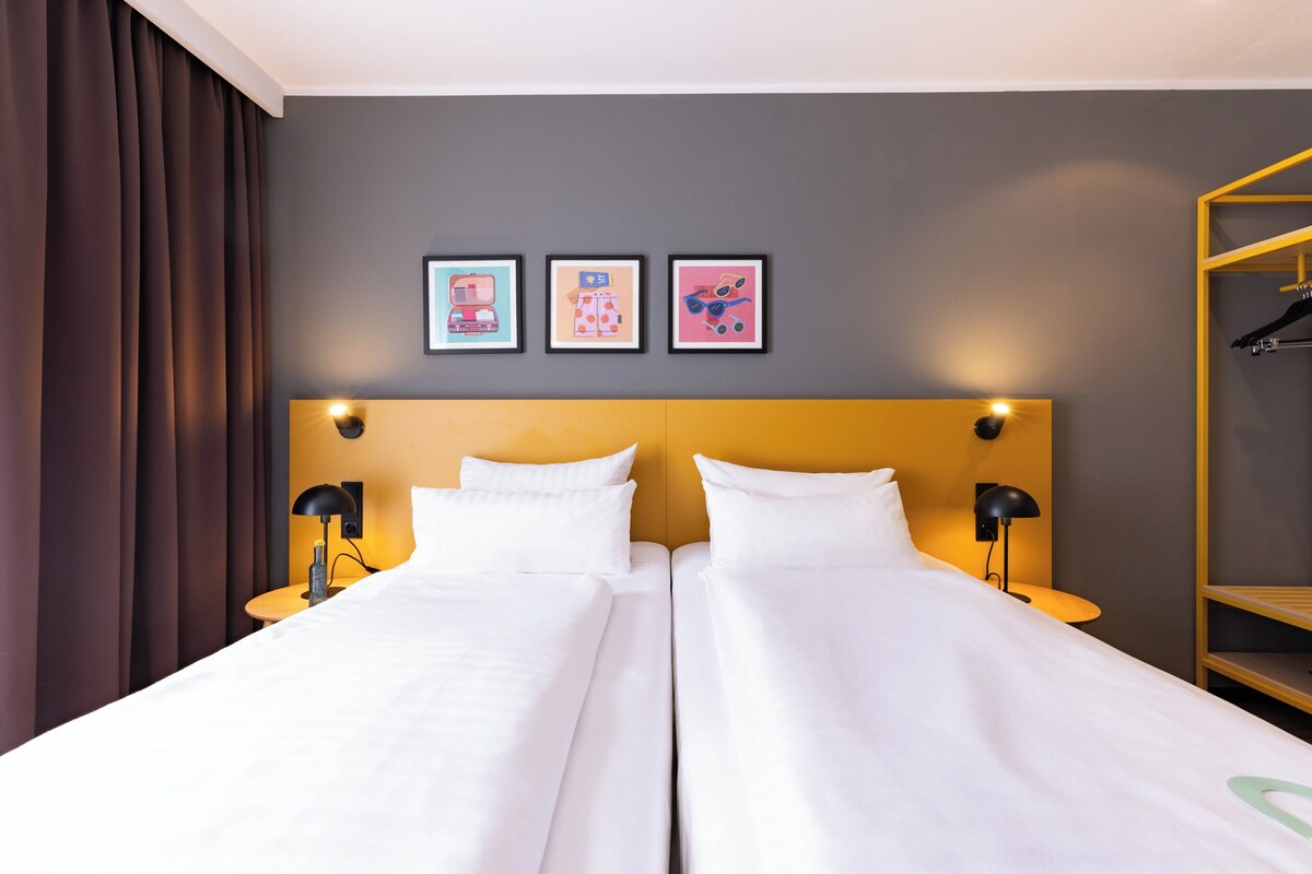 A hotel room with two beds, a wooden headboard, and a wardrobe with a yellow frame.