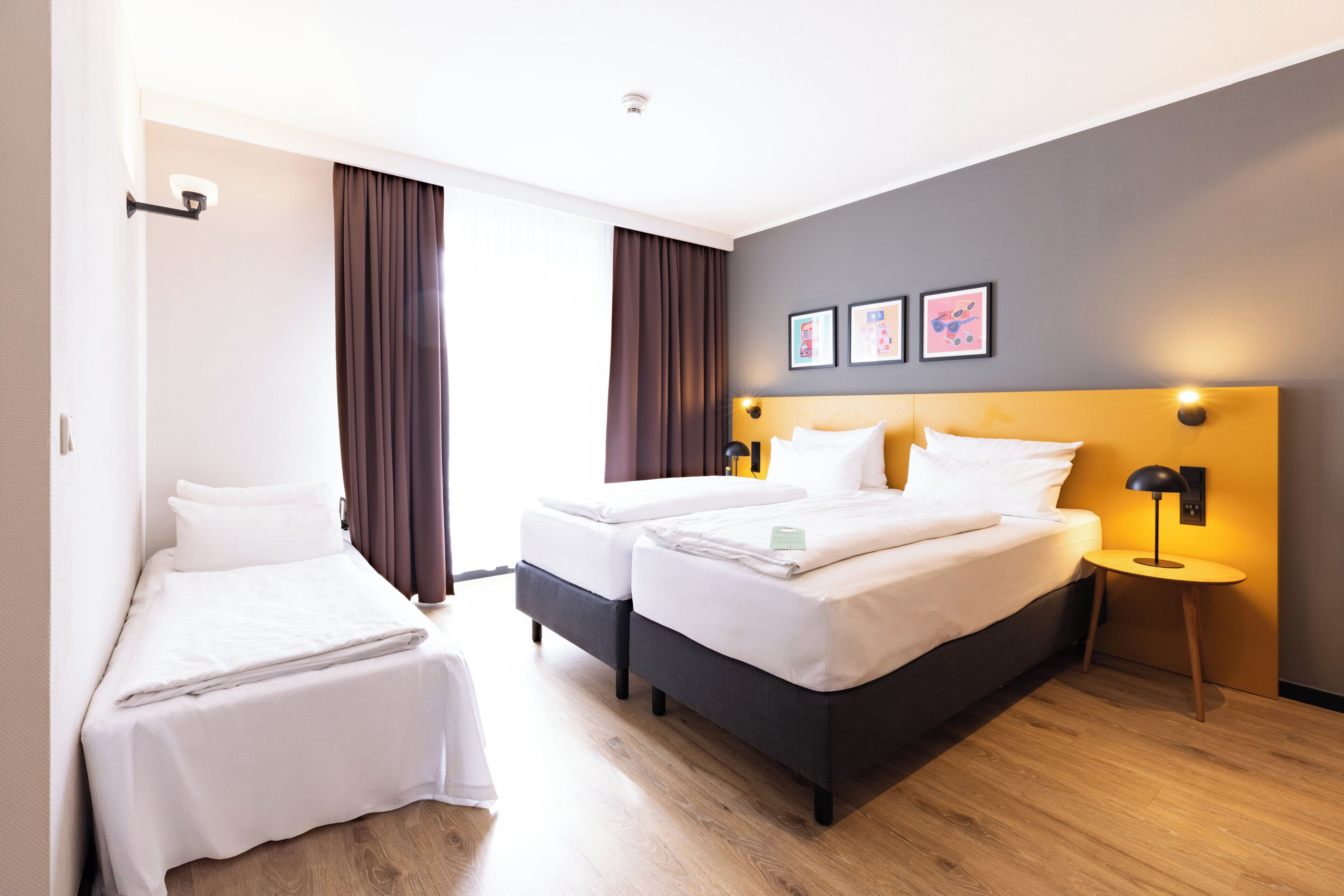 A hotel room with two beds, a bedside table with a lamp, and a wall-mounted picture.