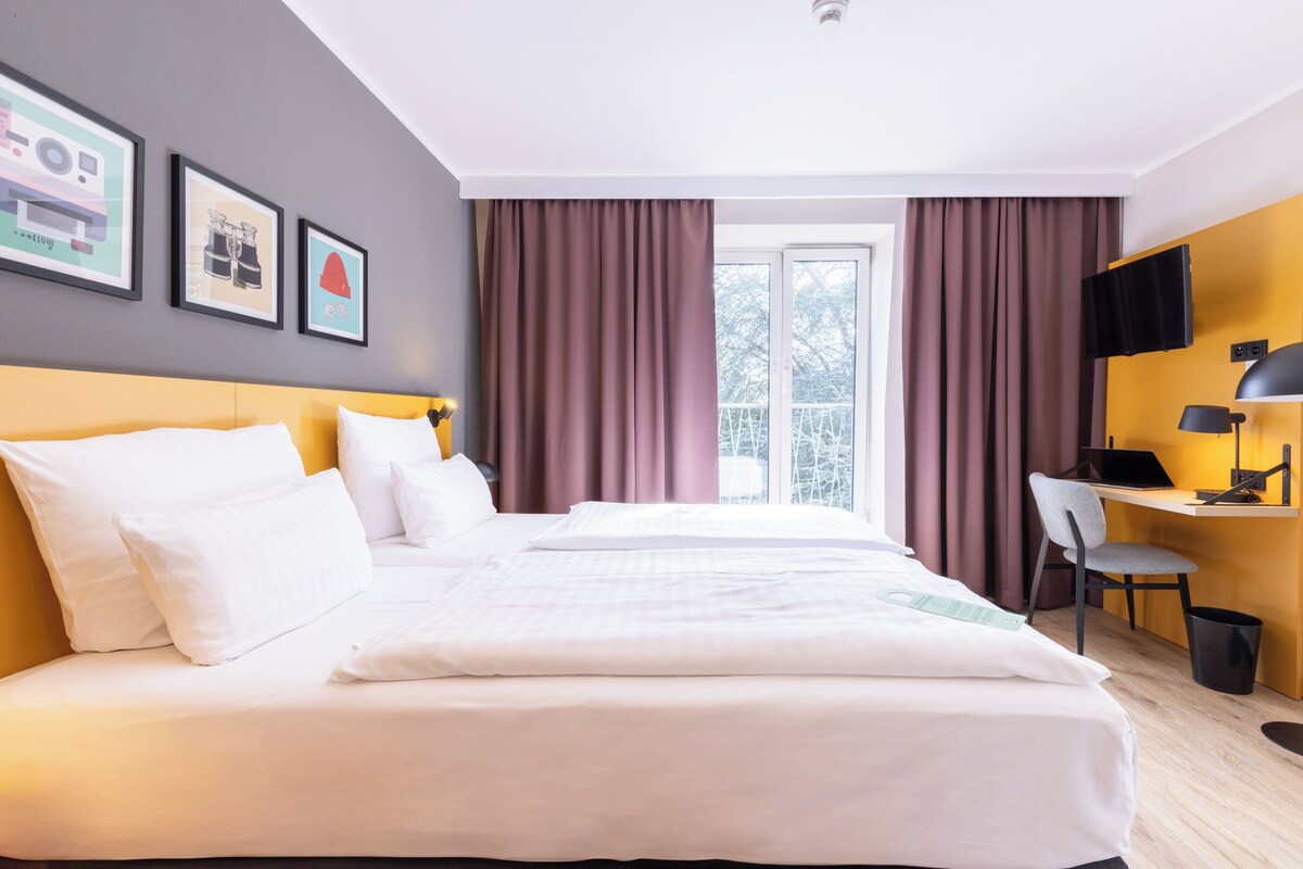A hotel room with a large bed, a desk with a chair, a TV, and a window with curtains.