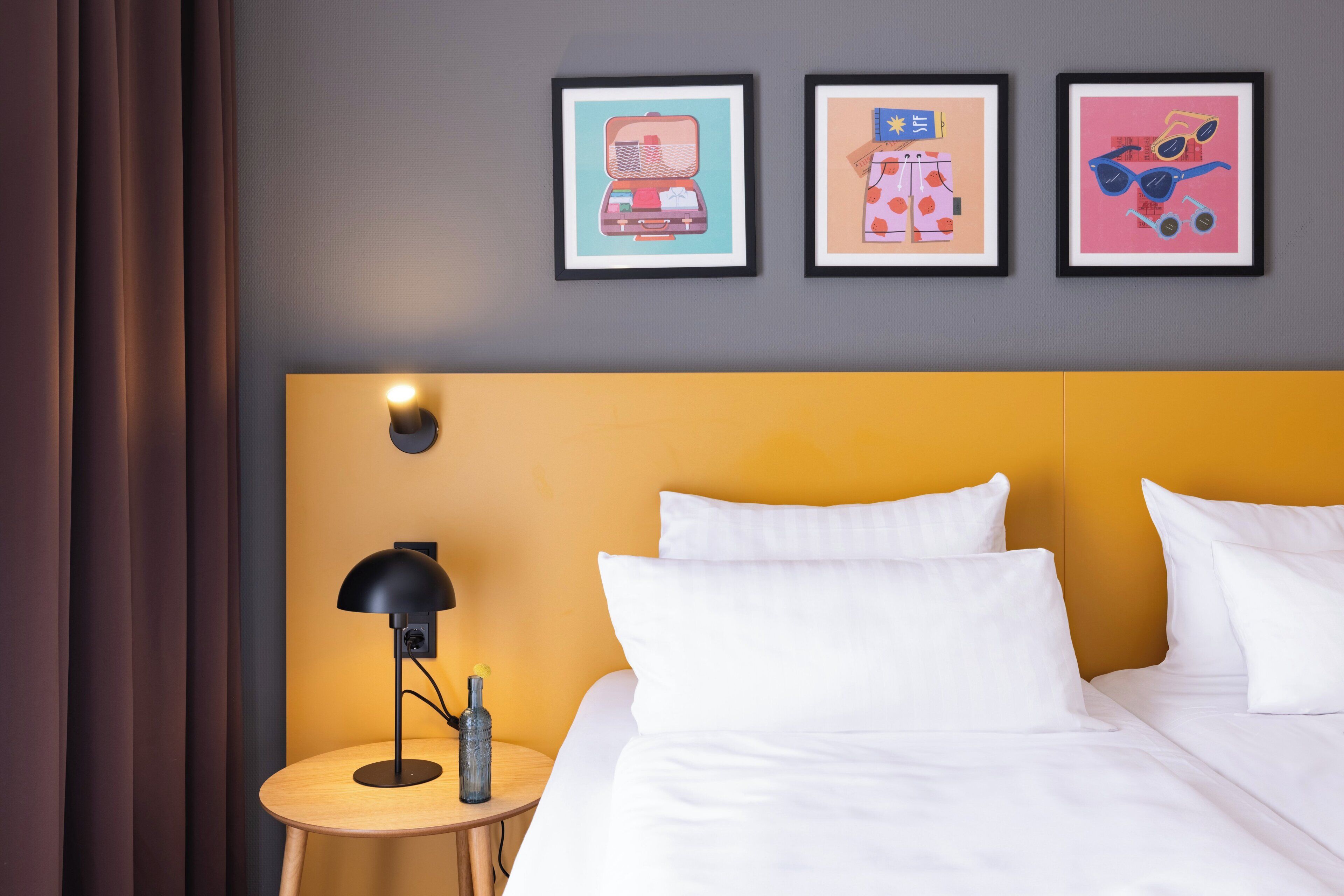 Habitación de hotel con cama, mesita de noche con lámpara y tres cuadros en la pared.