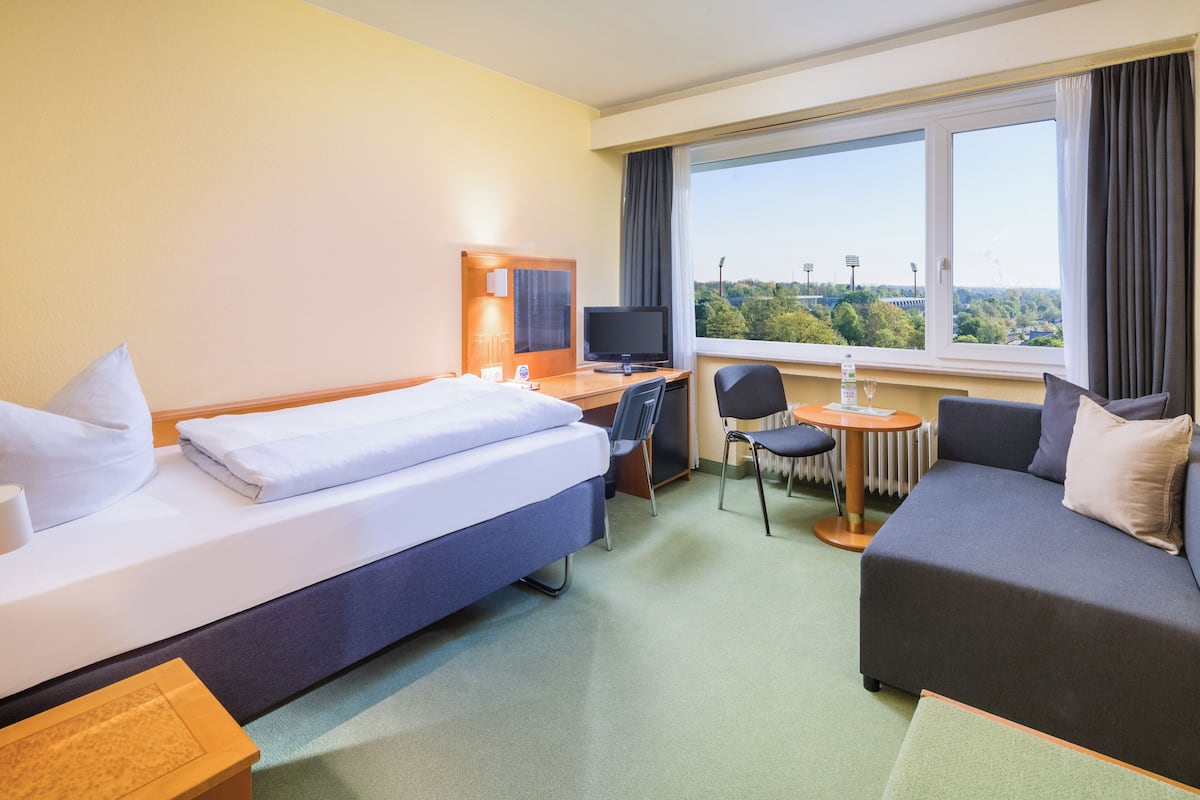 Una habitación de hotel con una cama, un escritorio con ordenador, una silla, un sofá y una ventana con vistas a la ciudad.