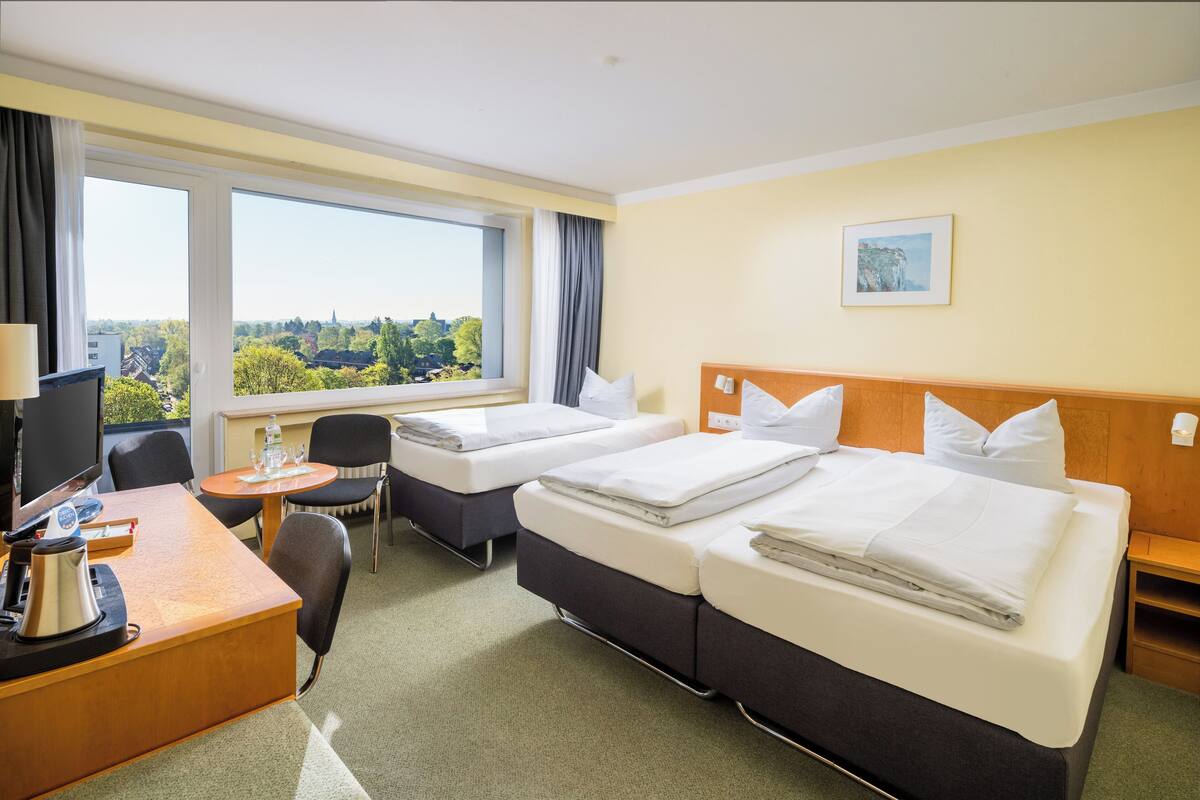 Habitación de hotel con dos camas, un escritorio con computadora, una silla y vista a la ciudad.