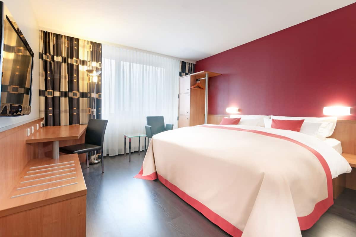 A hotel room with a bed, desk, chair, and a wardrobe.