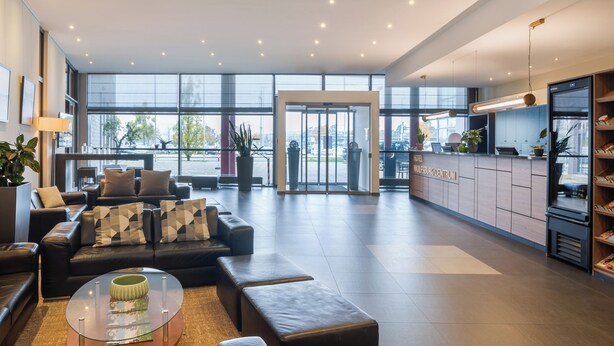 A modern hotel lobby with a leather sofa, a glass coffee table, and a reception desk. - Hotel Wolfsburg Centrum, Affiliated by Meliá (Wolfsburg)