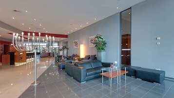 Un moderno hall de hotel con zona de estar, mostrador de recepción y una planta grande.