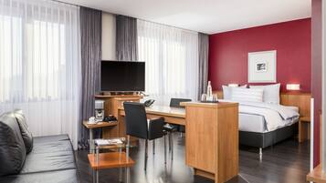 A modern hotel room with a bed, a desk, a sofa, and a TV.