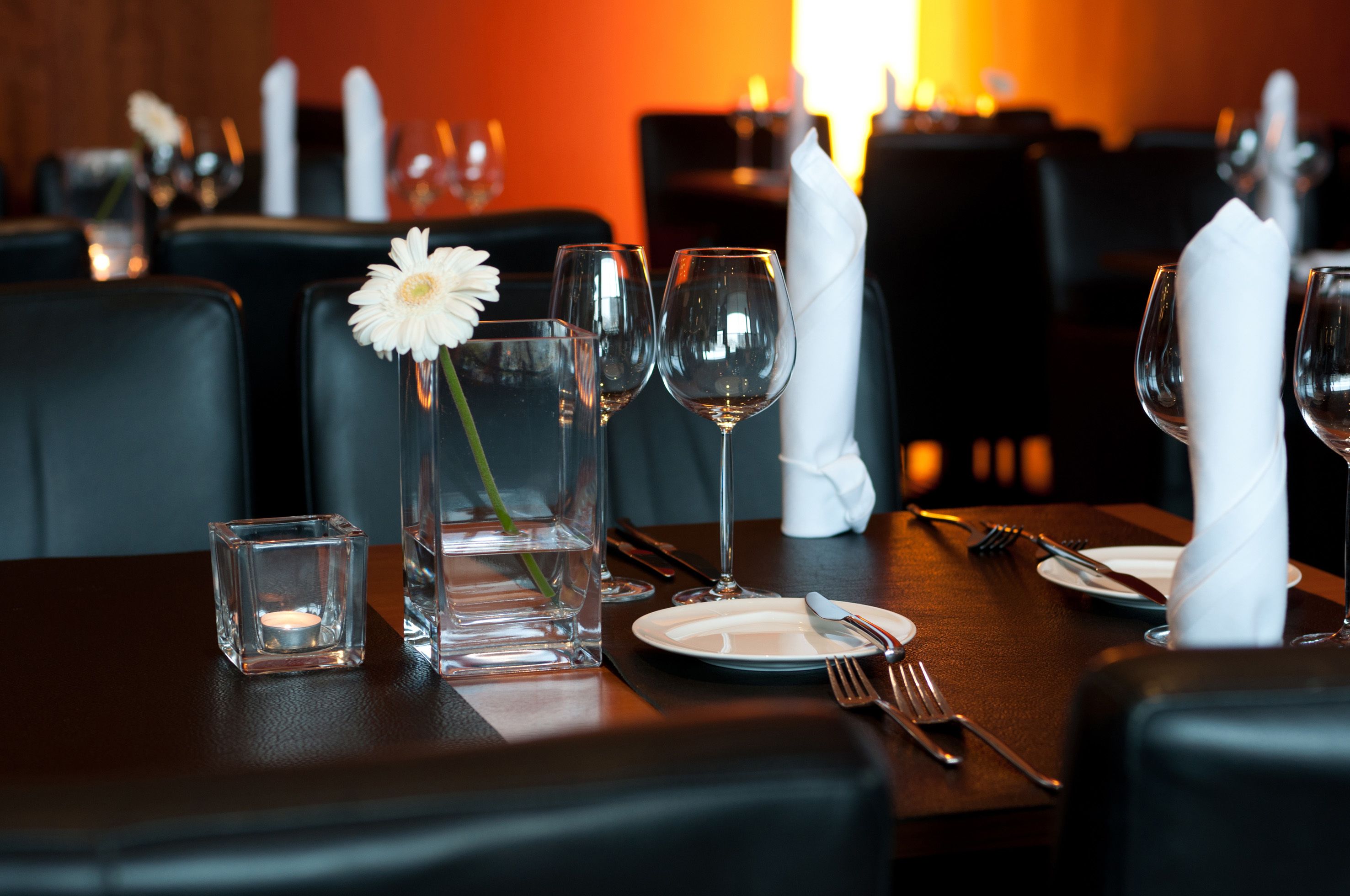Une table de restaurant dressée avec des verres à vin, une bougie et une fleur dans un vase en verre.
