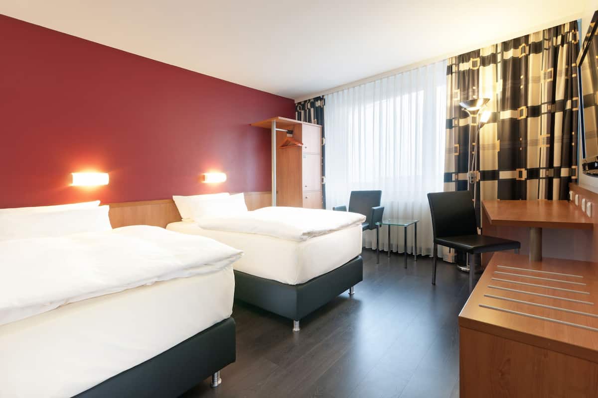 A hotel room with two beds, a desk, a chair, a wardrobe, and a dining area.