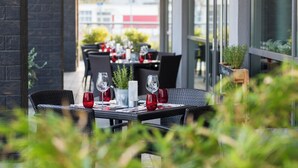 An outdoor dining area with tables set for two, featuring red glassware and a potted plant. - Hotel Wolfsburg Centrum, Affiliated by Meliá (Wolfsburg)