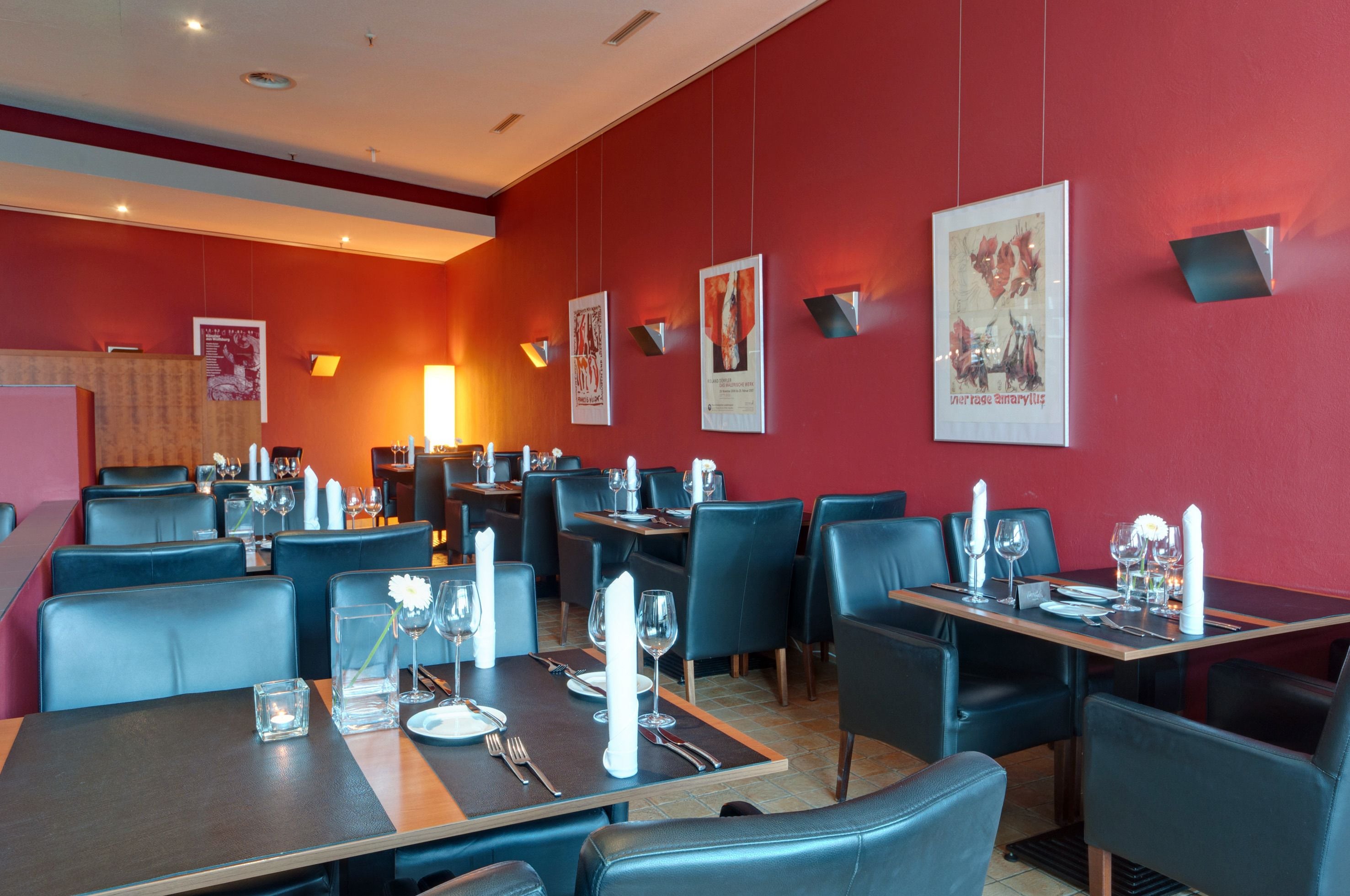 Ein Restaurant mit roten Wänden, schwarzen Ledersesseln und Tischen, die mit weißen Servietten und Besteck gedeckt sind.