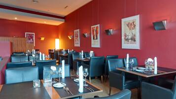 Ein Restaurant mit roten Wänden, schwarzen Ledersesseln und Tischen, die mit weißen Servietten und Besteck gedeckt sind.