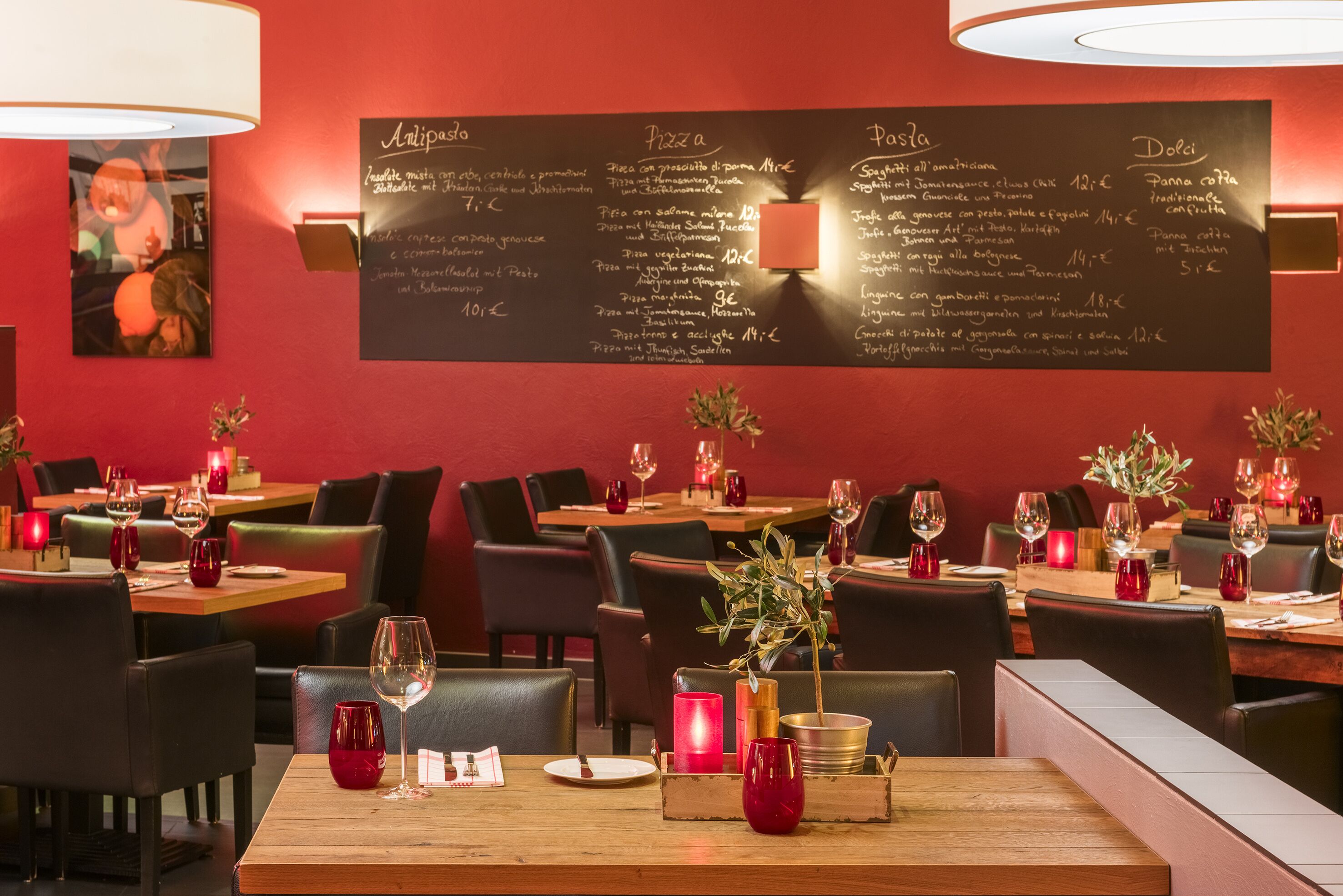 A restaurant interior with tables set for dining, a menu on the wall, and candles on the tables.