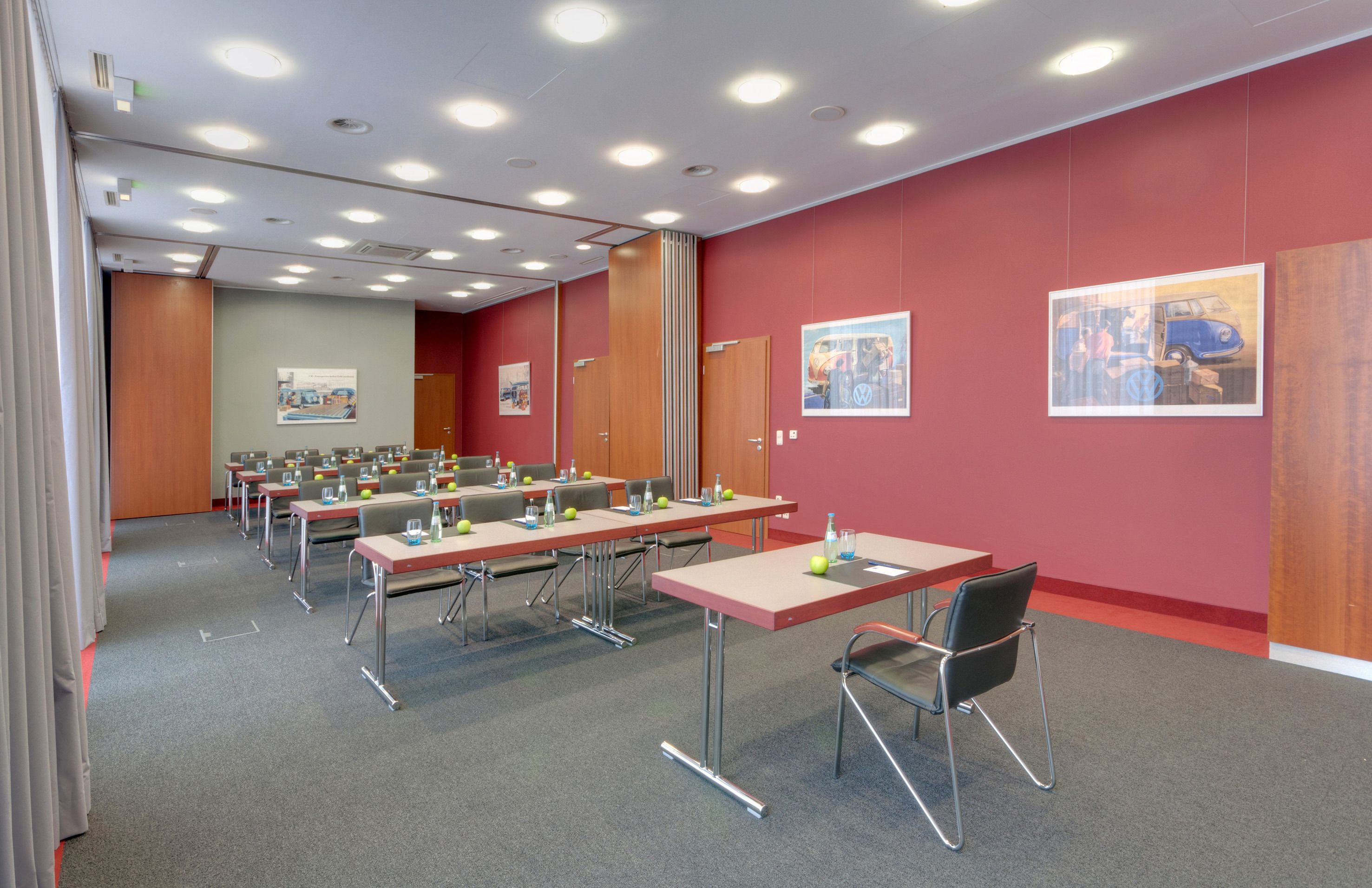 A conference room with multiple tables, chairs, and a red wall with framed pictures.