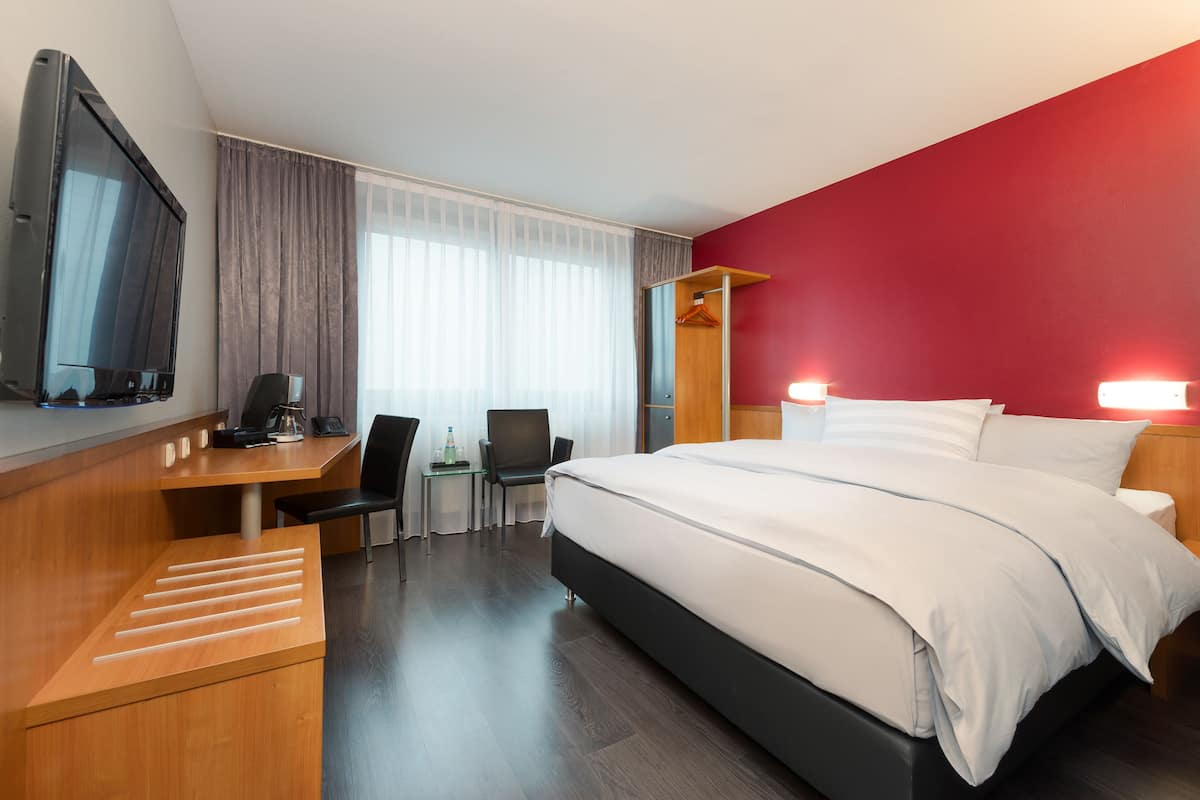A hotel room with a bed, desk, chair, and a television.