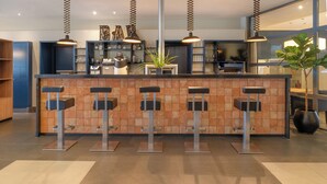 A modern bar area with a central column, four bar stools, and pendant lighting. - Hotel Wolfsburg Centrum, Affiliated by Meliá (Wolfsburg)