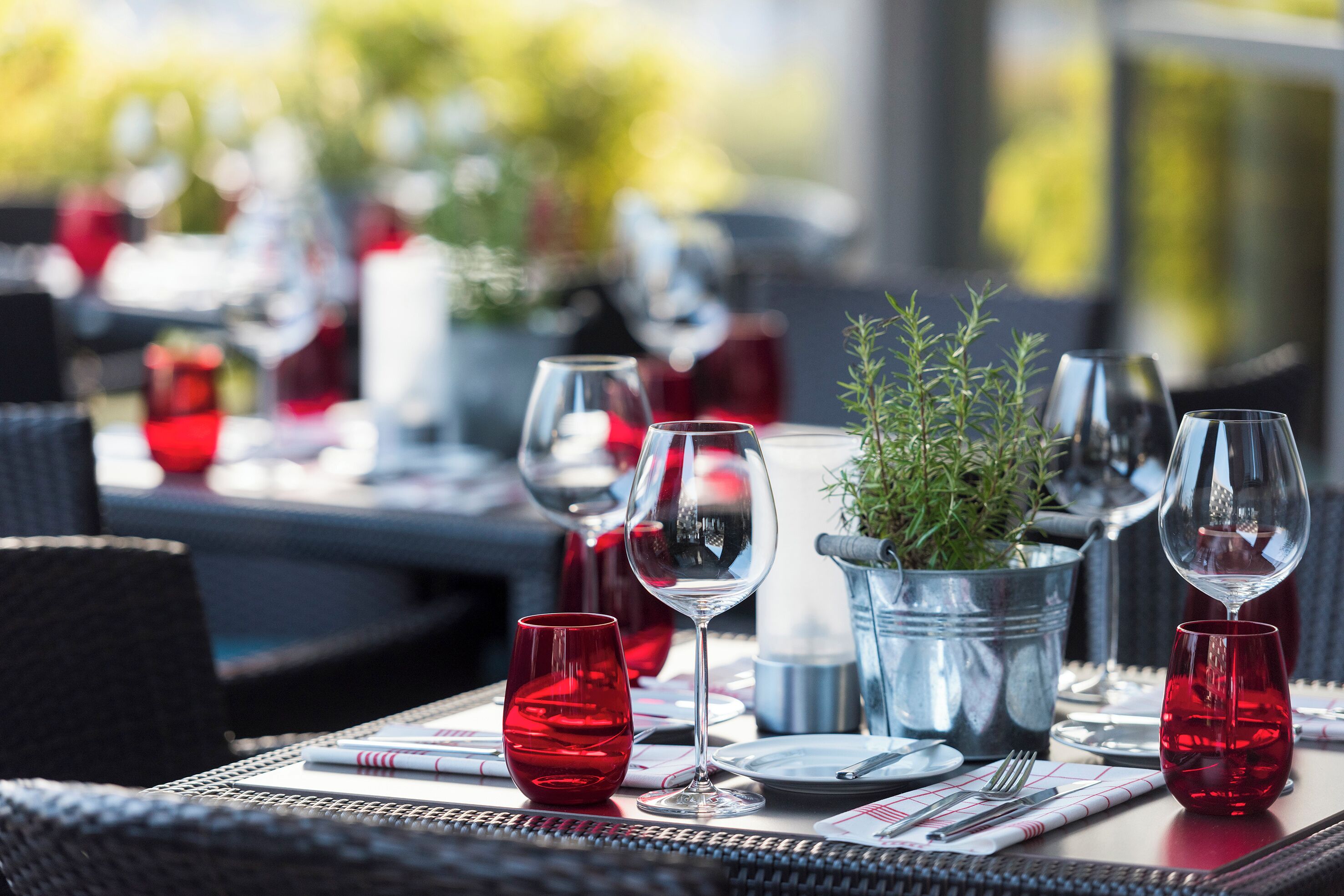 A dining table set with red glasses, a silver bucket, and a potted plant.