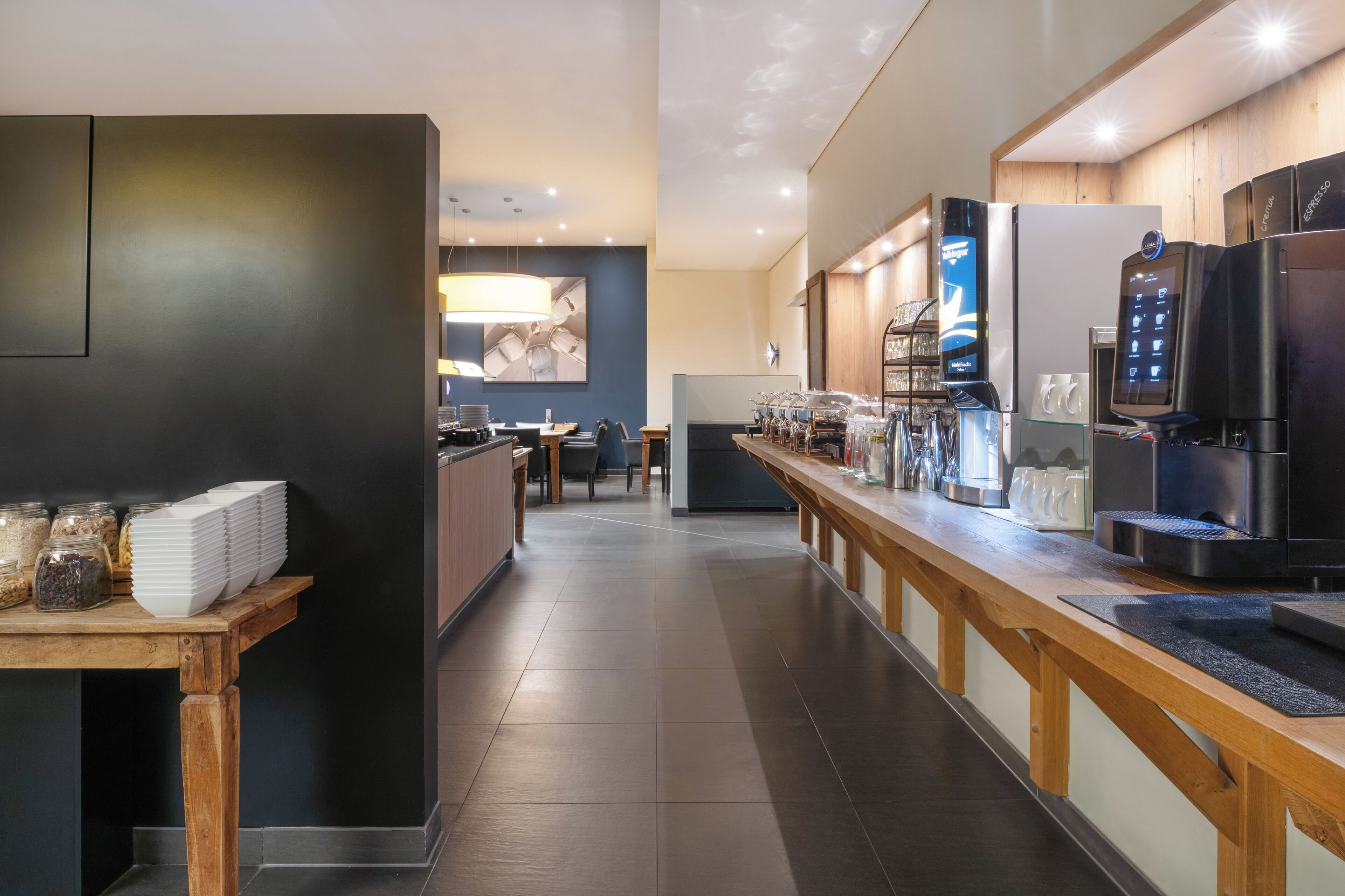 A modern kitchen with a long counter, espresso machines, and a coffee station.