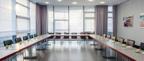 A conference room with a long table, chairs, and a large window with curtains.